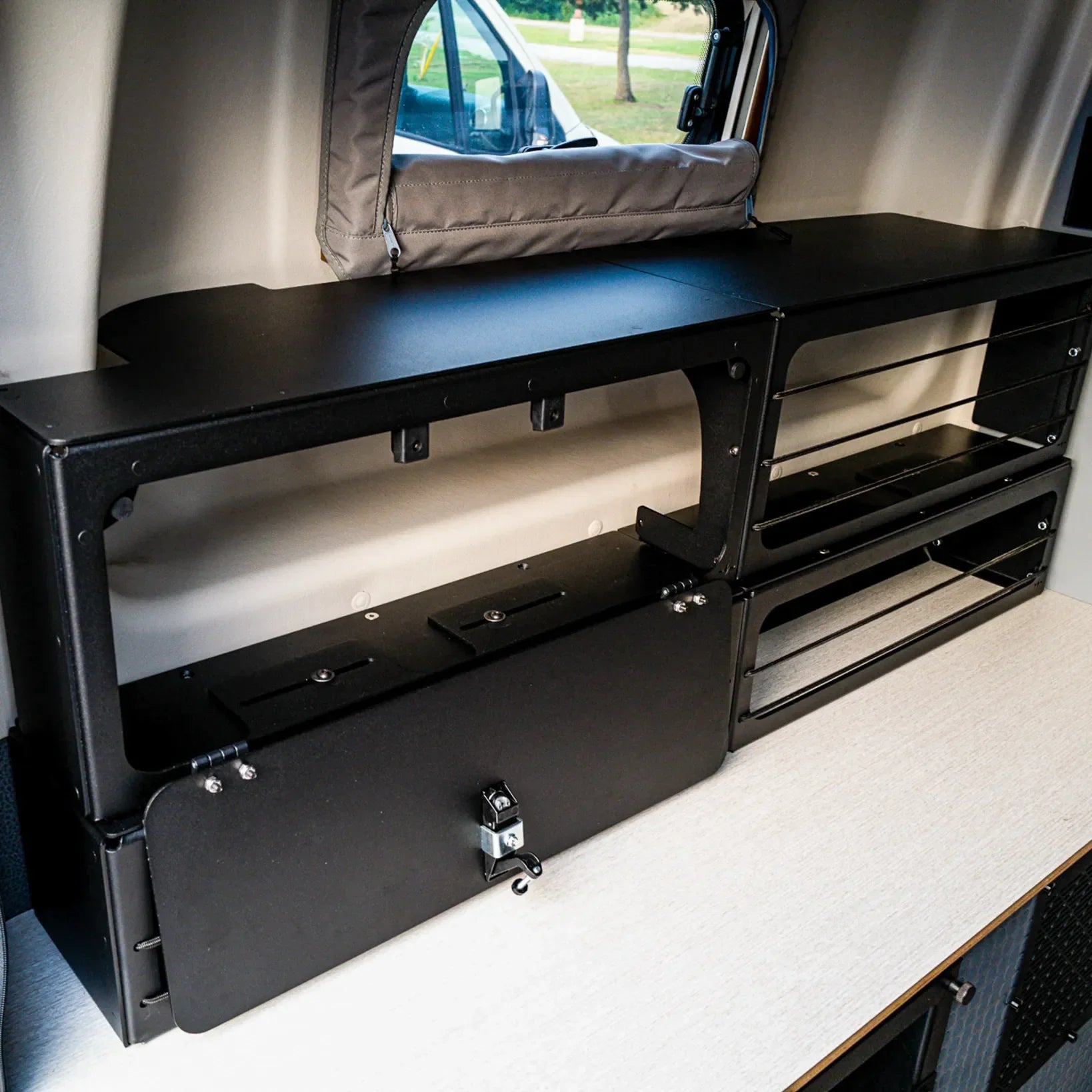 Black Pro Series bed risers with bungee cords and lower storage box installed inside a Winnebago Revel van.