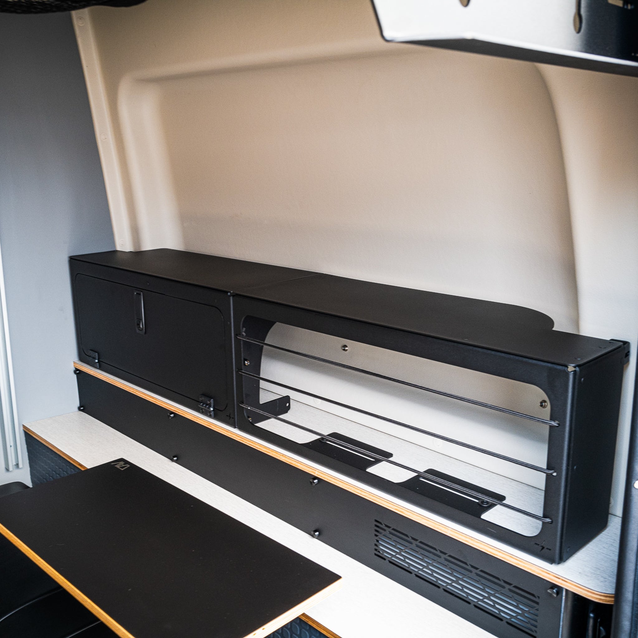 Black lower storage box and bed risers installed in a Winnebago Revel van interior.