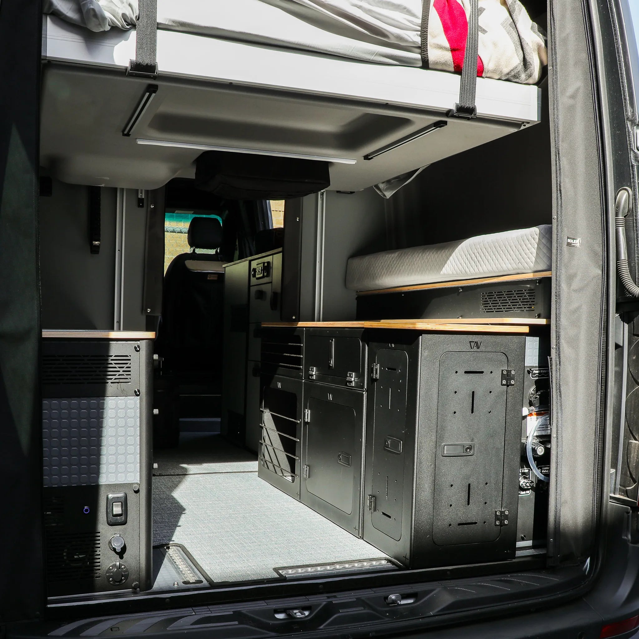 Rear view of GLSS Passenger PRO van interior with bed, desk area, and H2O box for 2025 Revel.