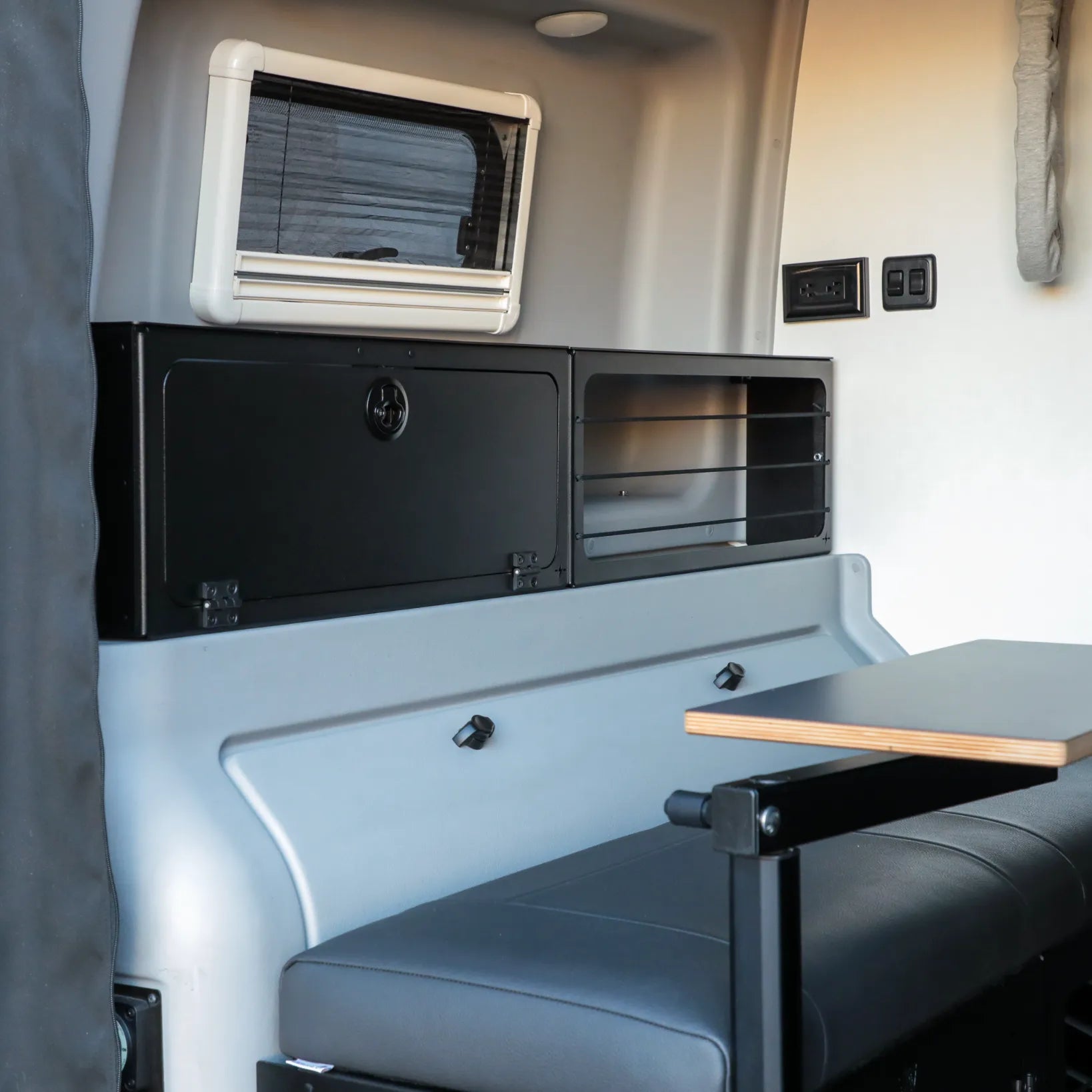 Revel van interior showing fold-down table, cushioned bench, and cabinet storage.
