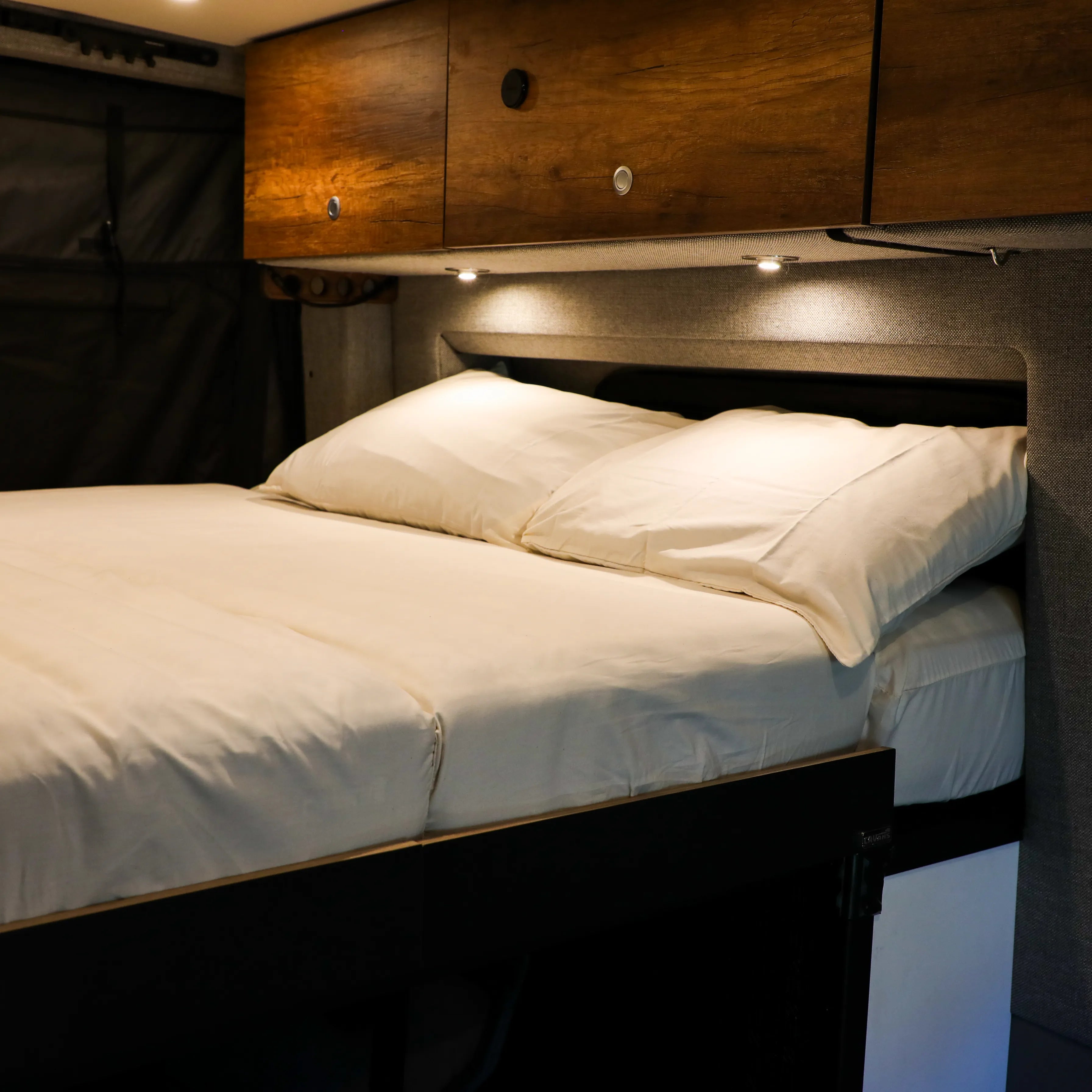 Storyteller Dream Bundle bed with white bedding in van interior under wood cabinets
