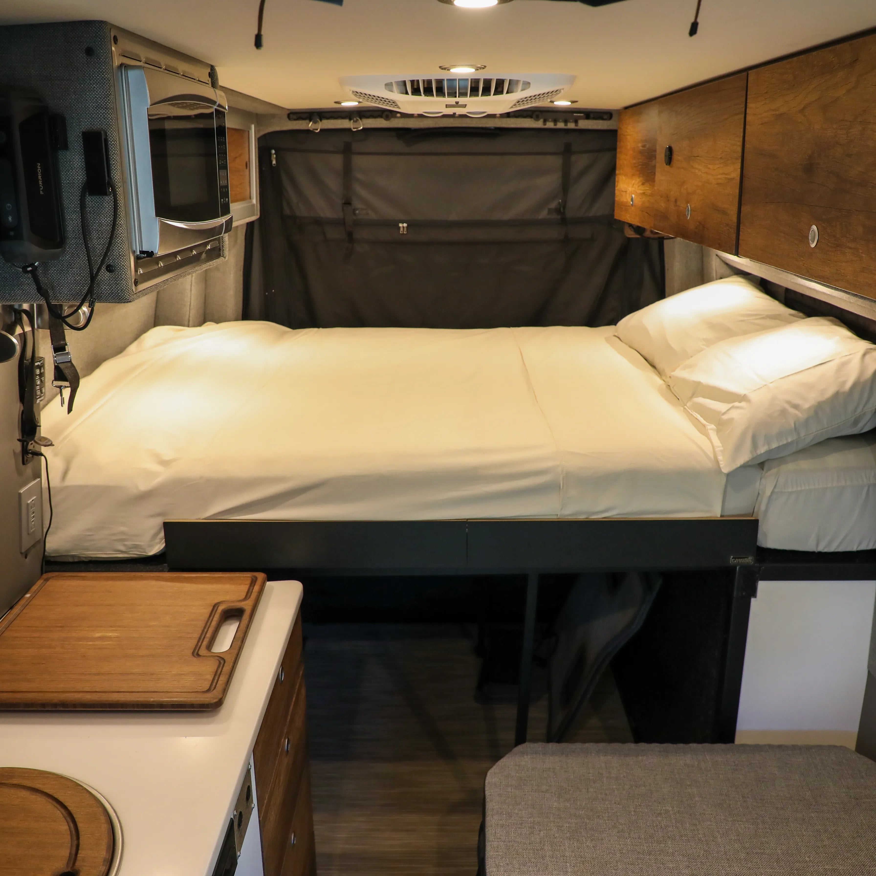Storyteller Overland Dream Bundle van interior with made bed, wood cabinets, and compact kitchen.