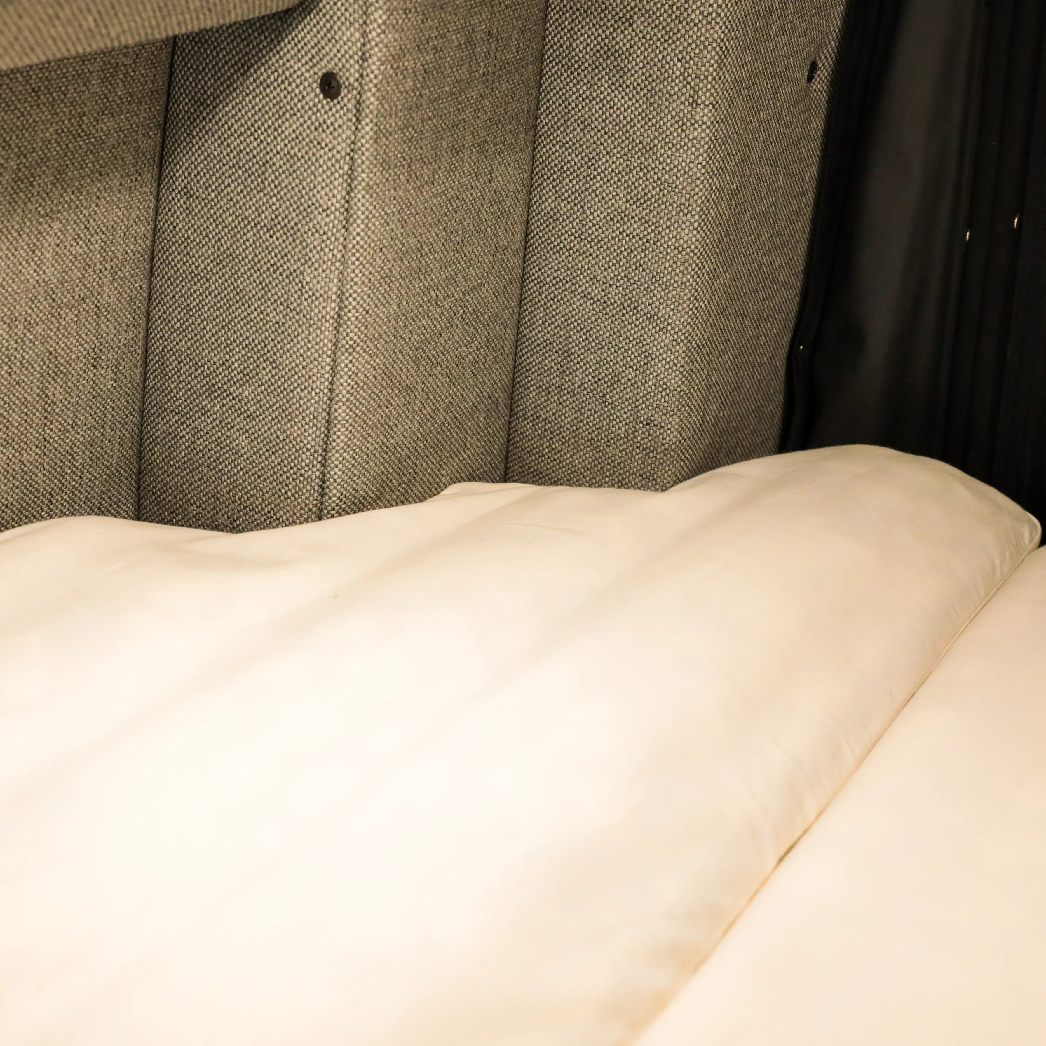 Close-up of a beige bed setup against gray padded wall inside a Storyteller Overland van.
