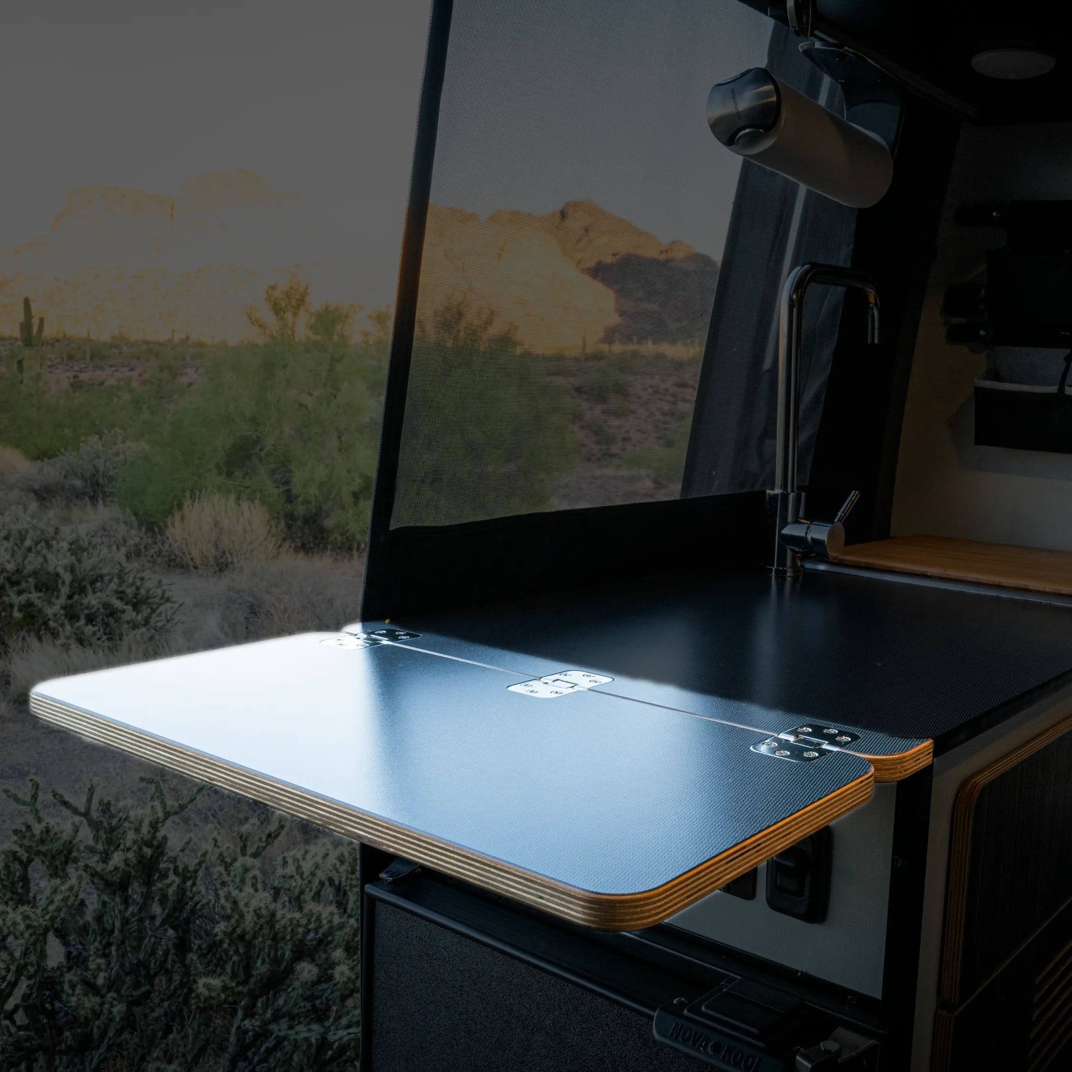Folding countertop extension installed in a Revel van kitchen with desert view outside.