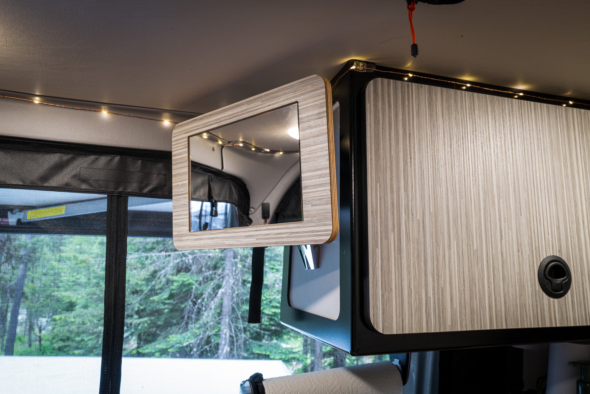 Canyon Mirror mounted inside a van near overhead cabinets and string lights.