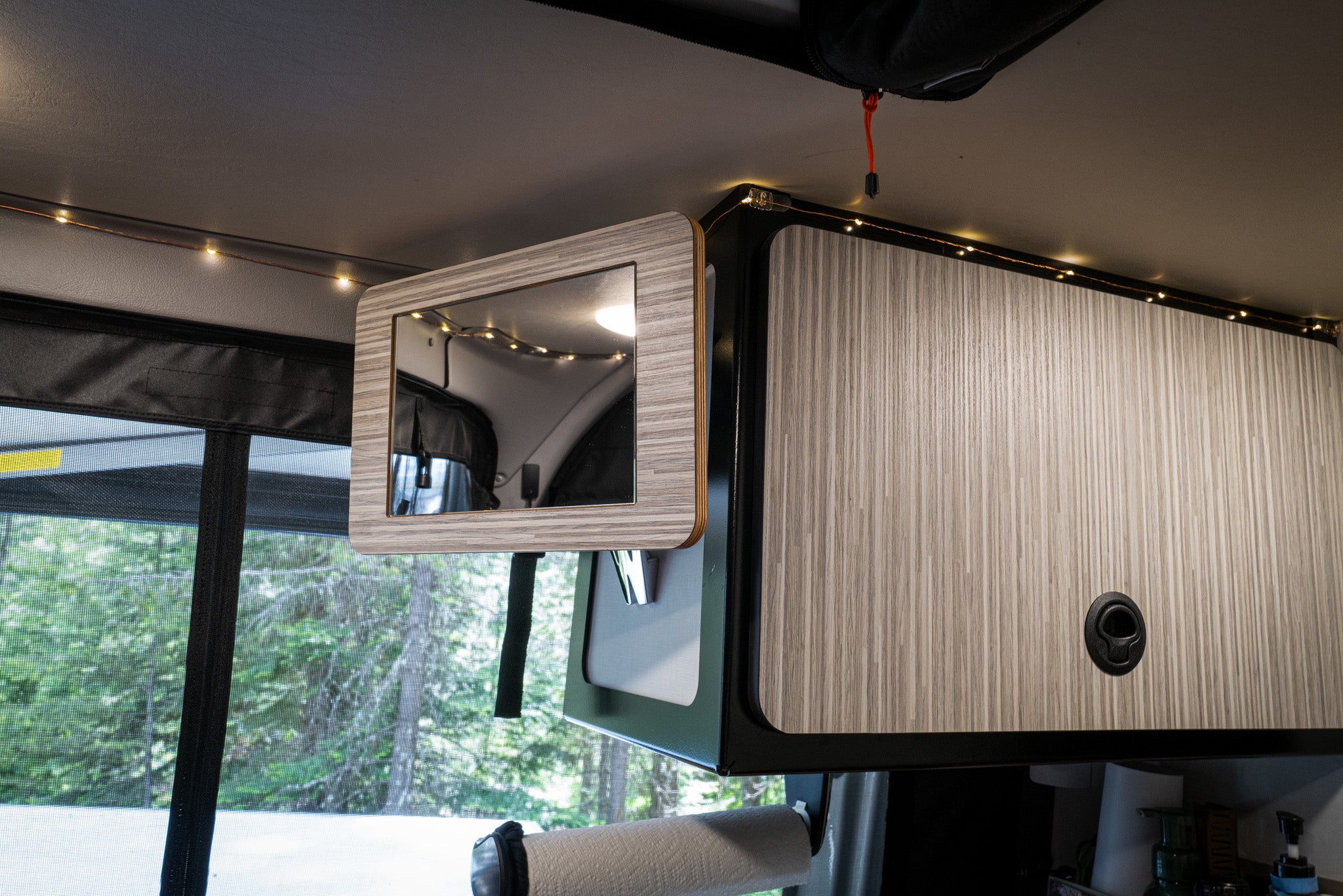 Canyon Mirror mounted on wood-paneled cabinet inside a van with ambient string lighting.