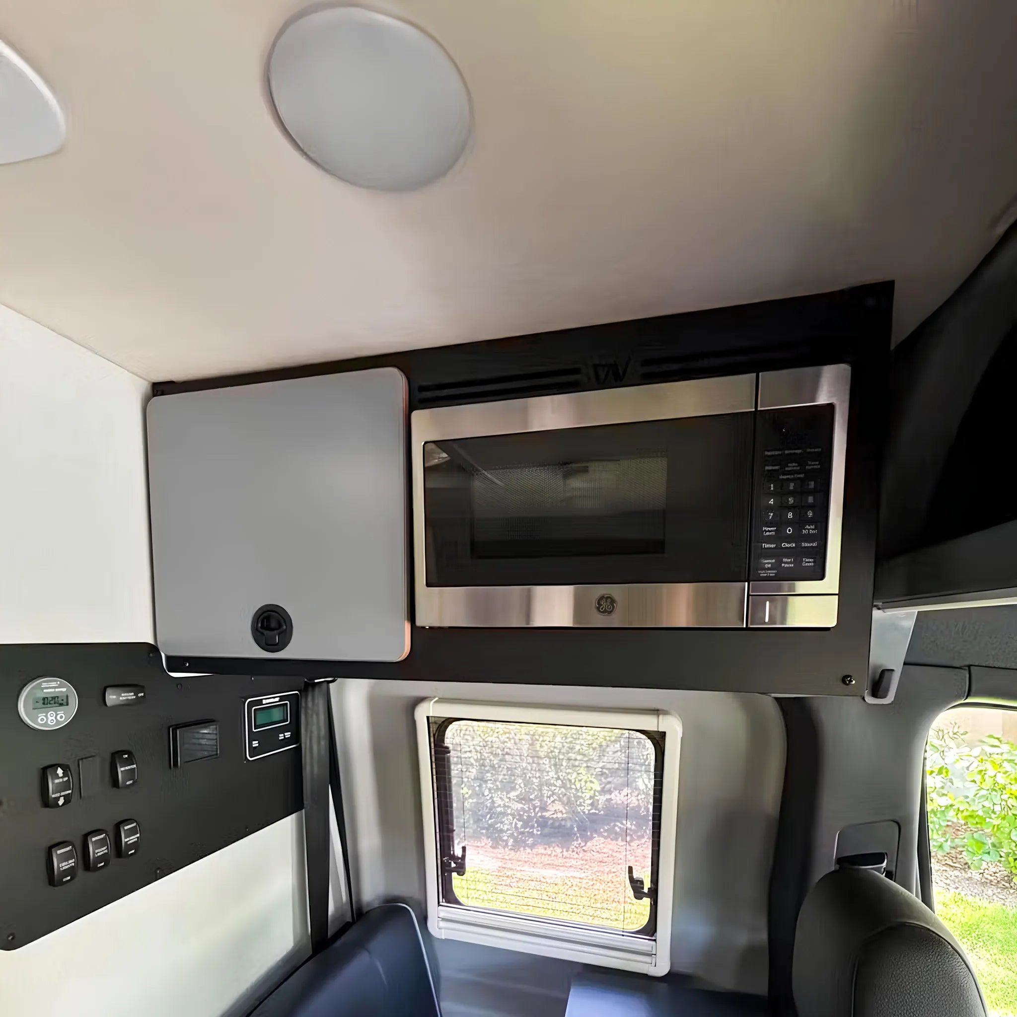 Microwave installed in upper cabinet of Revel van interior, positioned above the window and control panel.