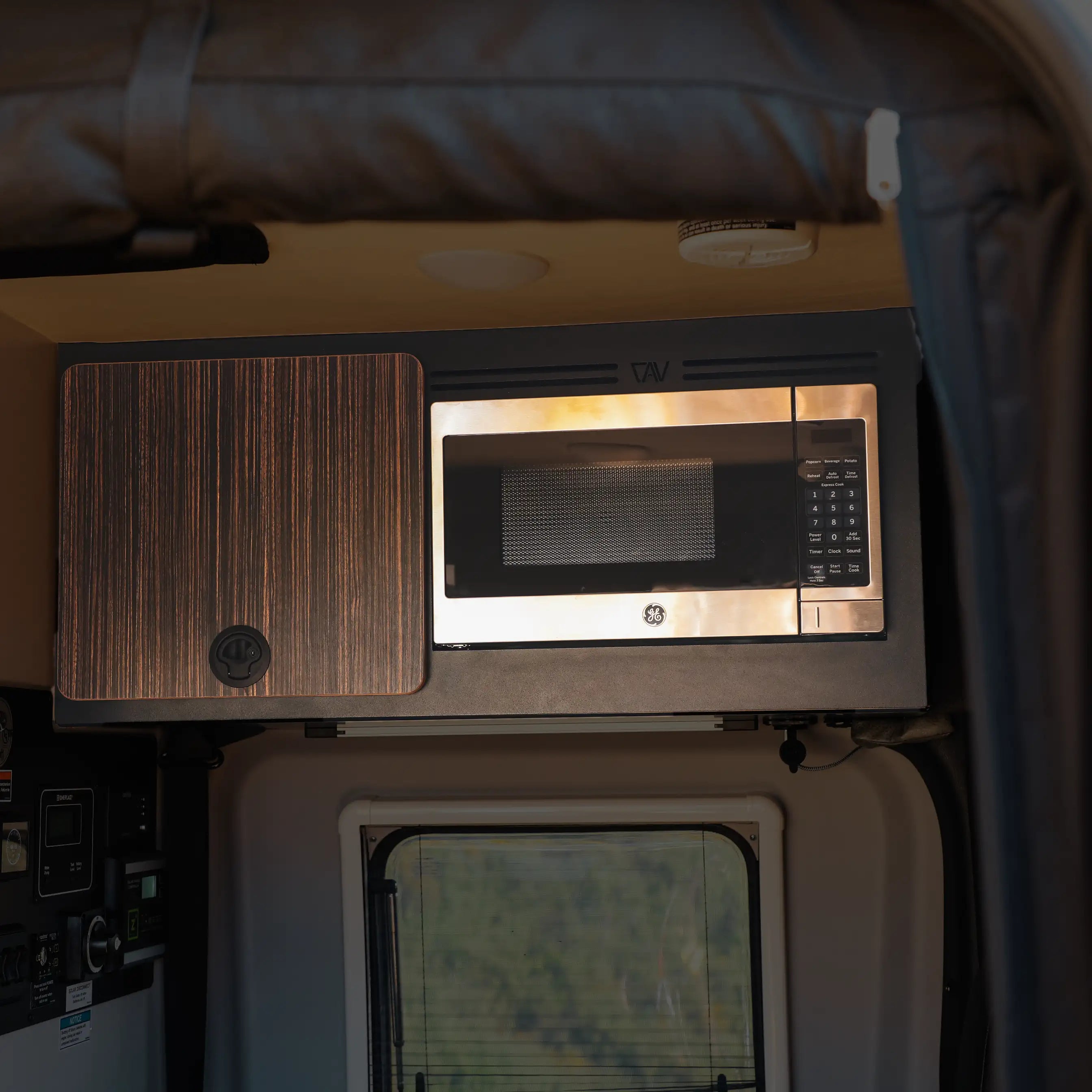 GE microwave installed in overhead cabinet kit inside a Revel van interior.