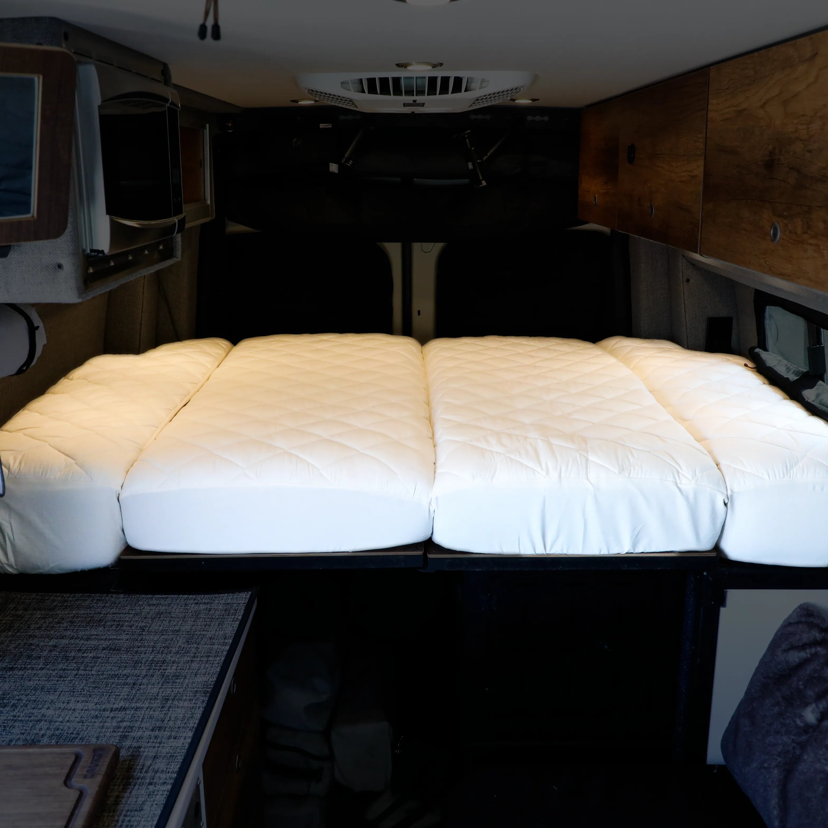 Ultra Luxe mattress protector pad laid out on extended bed platform inside a van interior.