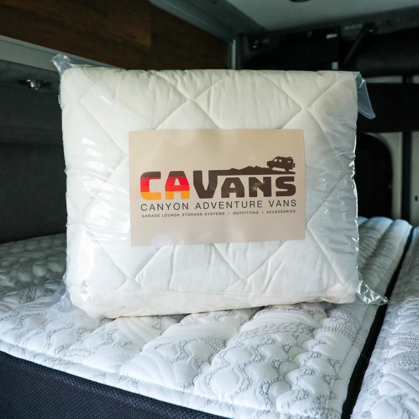 CAVans quilted bedding set in packaging, placed on a mattress inside a van interior.