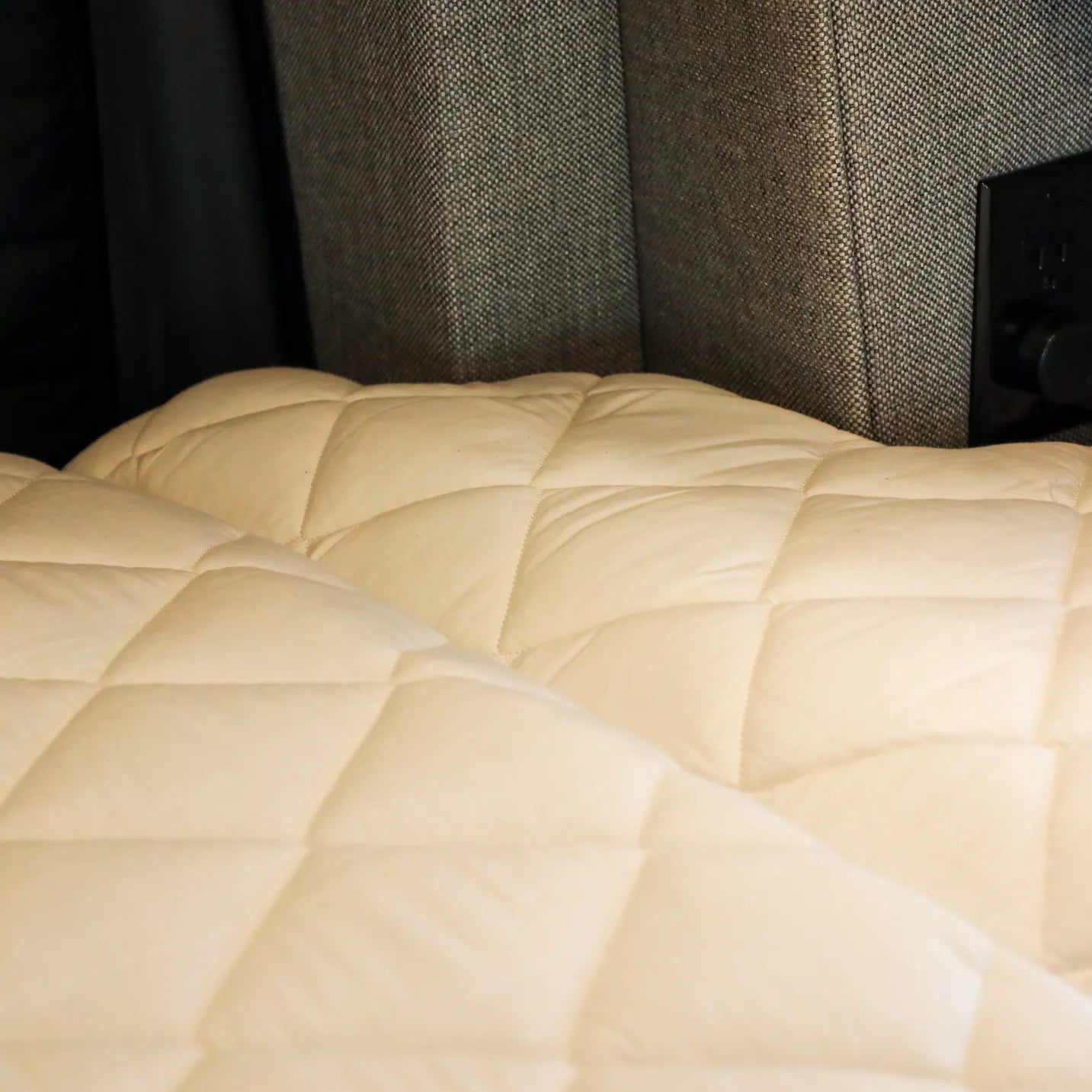 Quilted Dream Bundle mattress pad inside van with grey upholstered wall panels and power outlet visible.