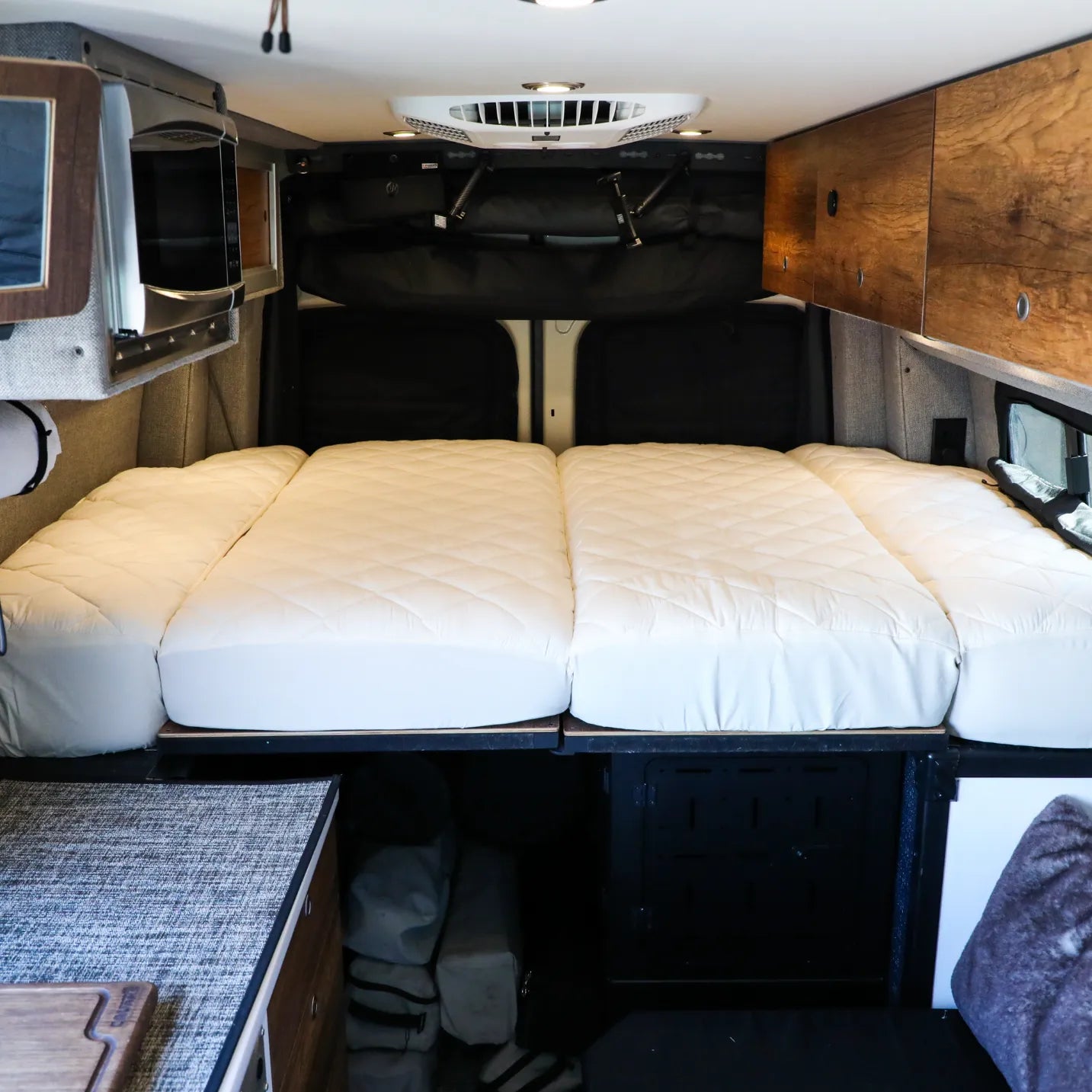 Interior of a Storyteller Overland van featuring a neatly made bed with quilted cushions.