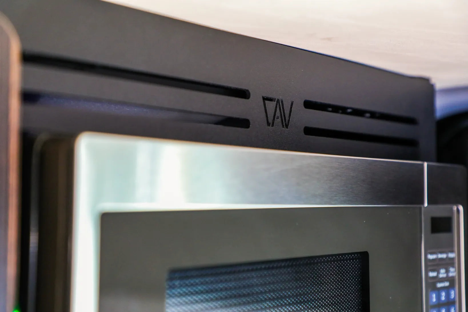 Close-up of mounted microwave in Revel van overhead cabinet kit, showing vent detail.
