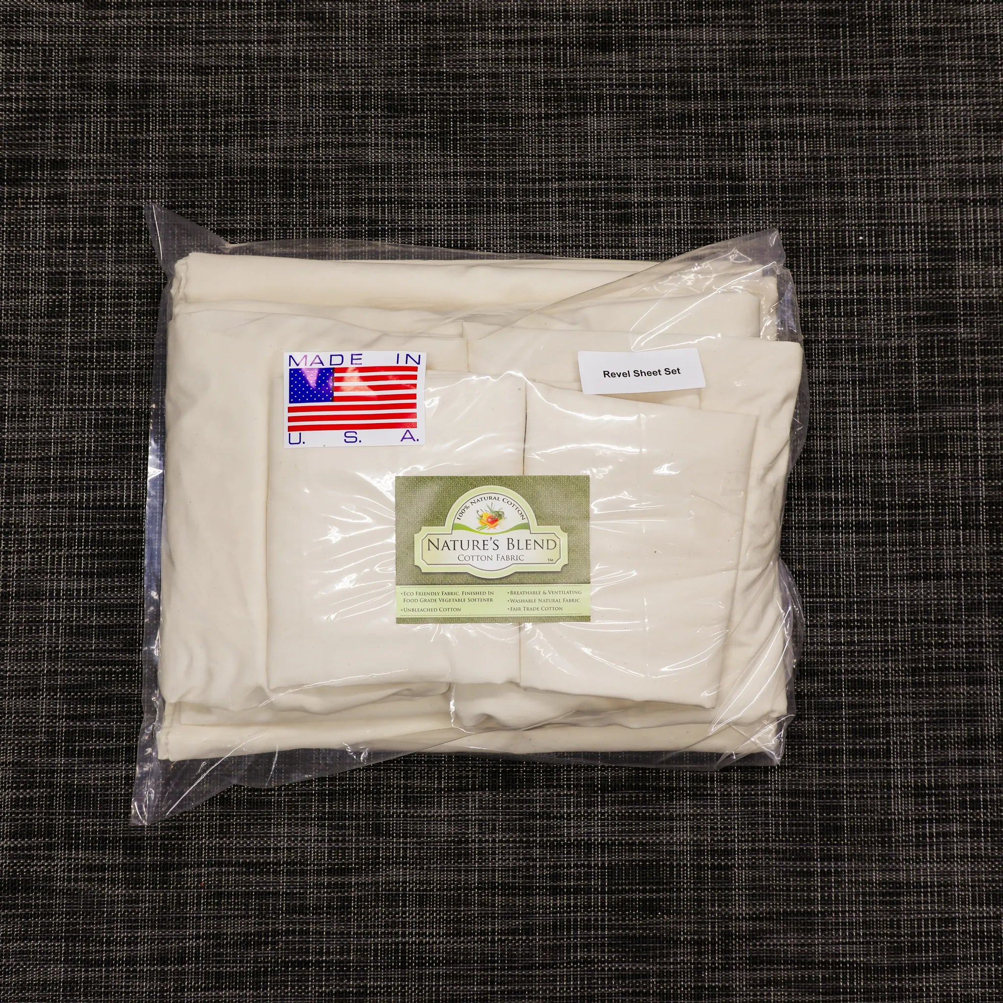 Revel sheet set in cream color, folded and packaged in clear plastic on dark fabric surface