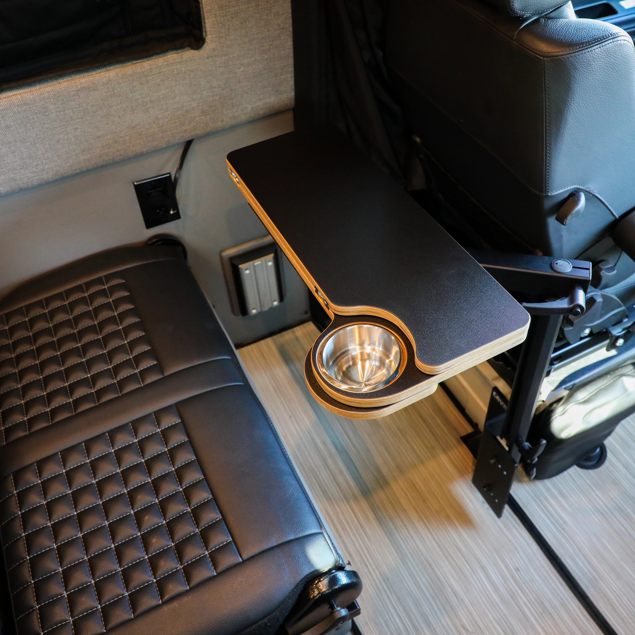 Carbon black folding console table with cup holder mounted between van seats in a Revel interior