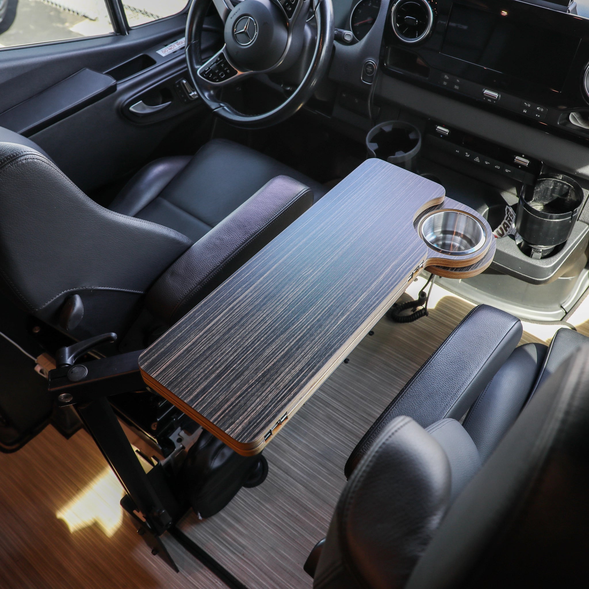 Solo Folding Table Top installed between driver and passenger seats in a van, featuring woodgrain finish and cup holder.