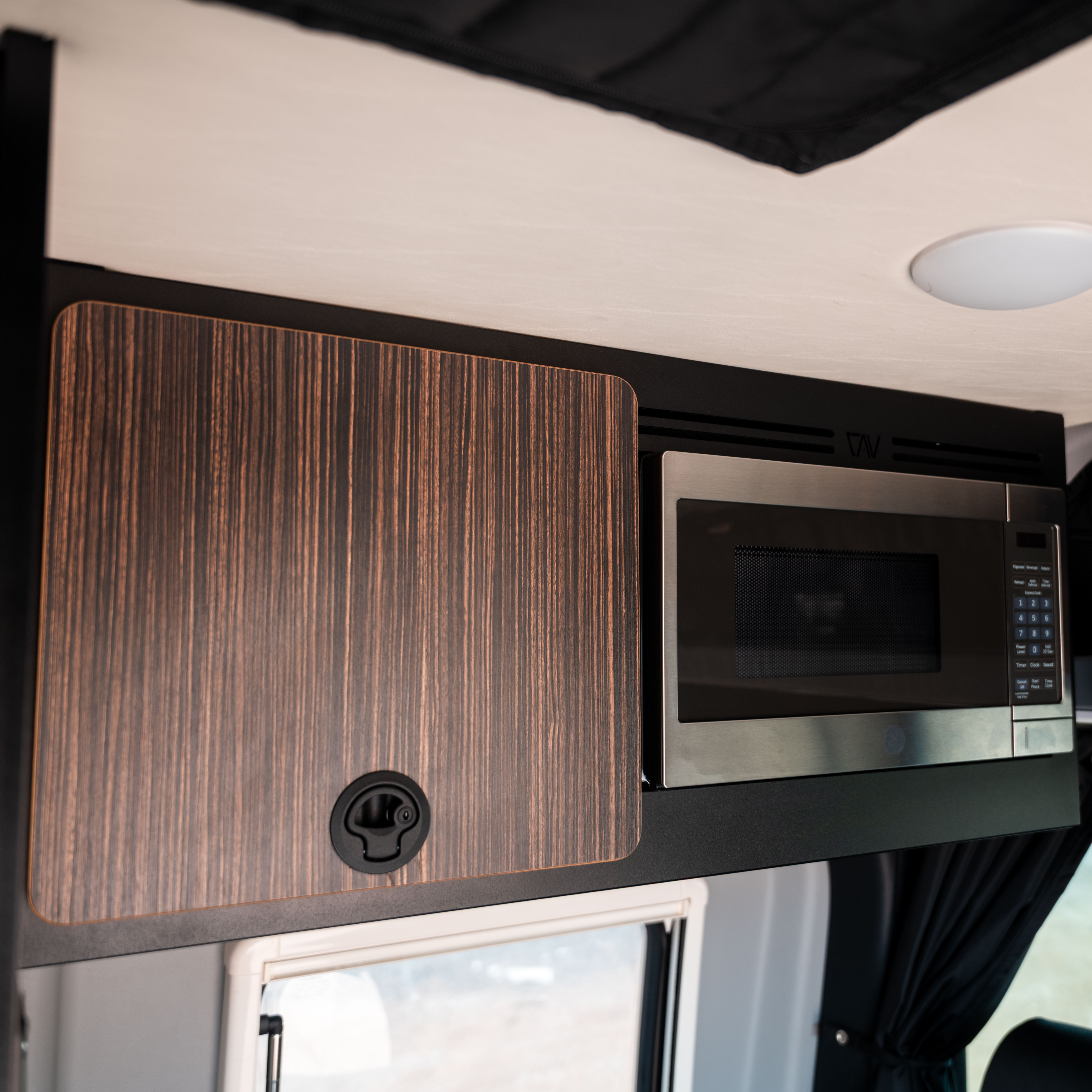 Microwave installed in overhead cabinet kit inside a Revel van from model years 2021 to 2024.