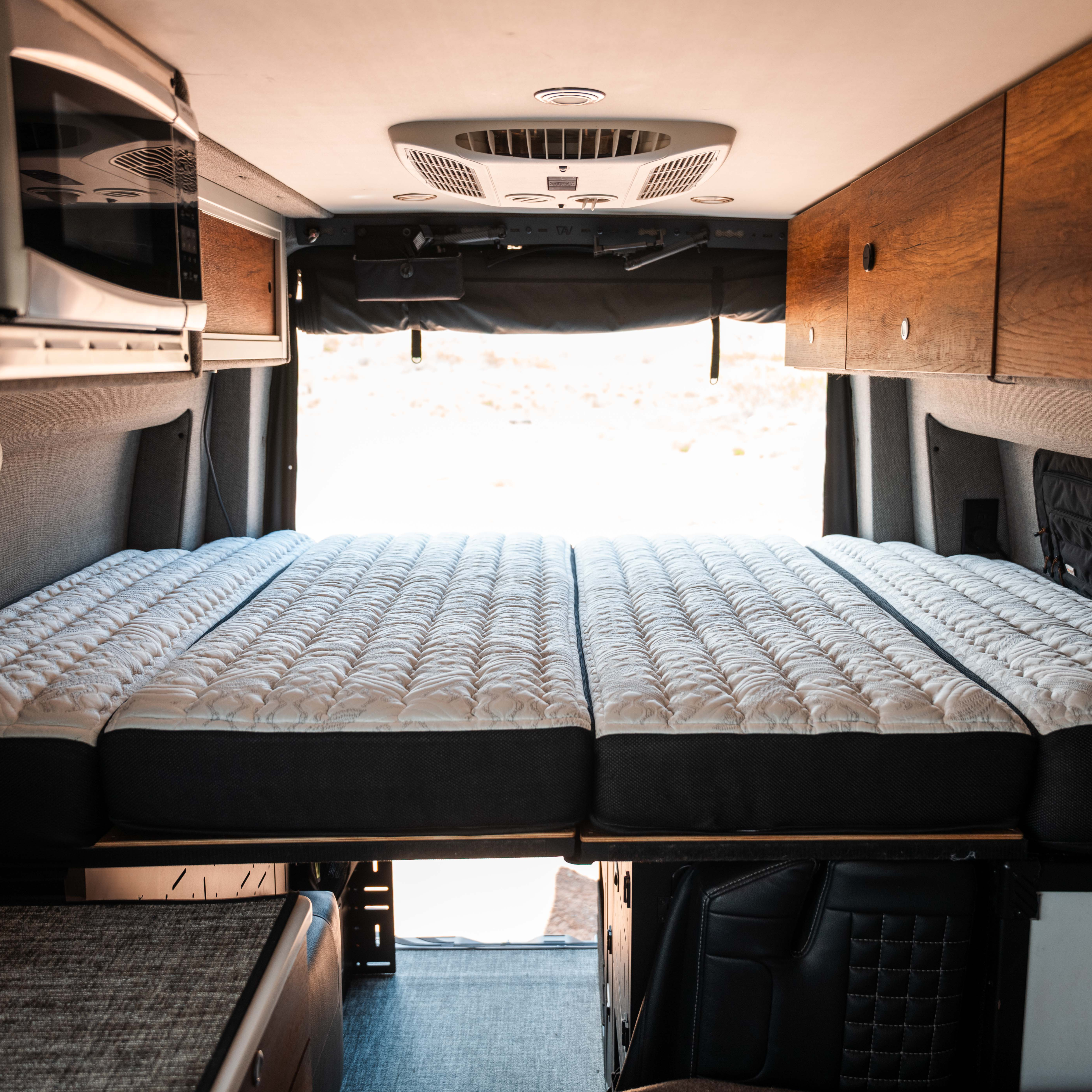 ULTRA Luxe Mattress by Storyteller Overland laid out in van interior with overhead storage and wood accents.