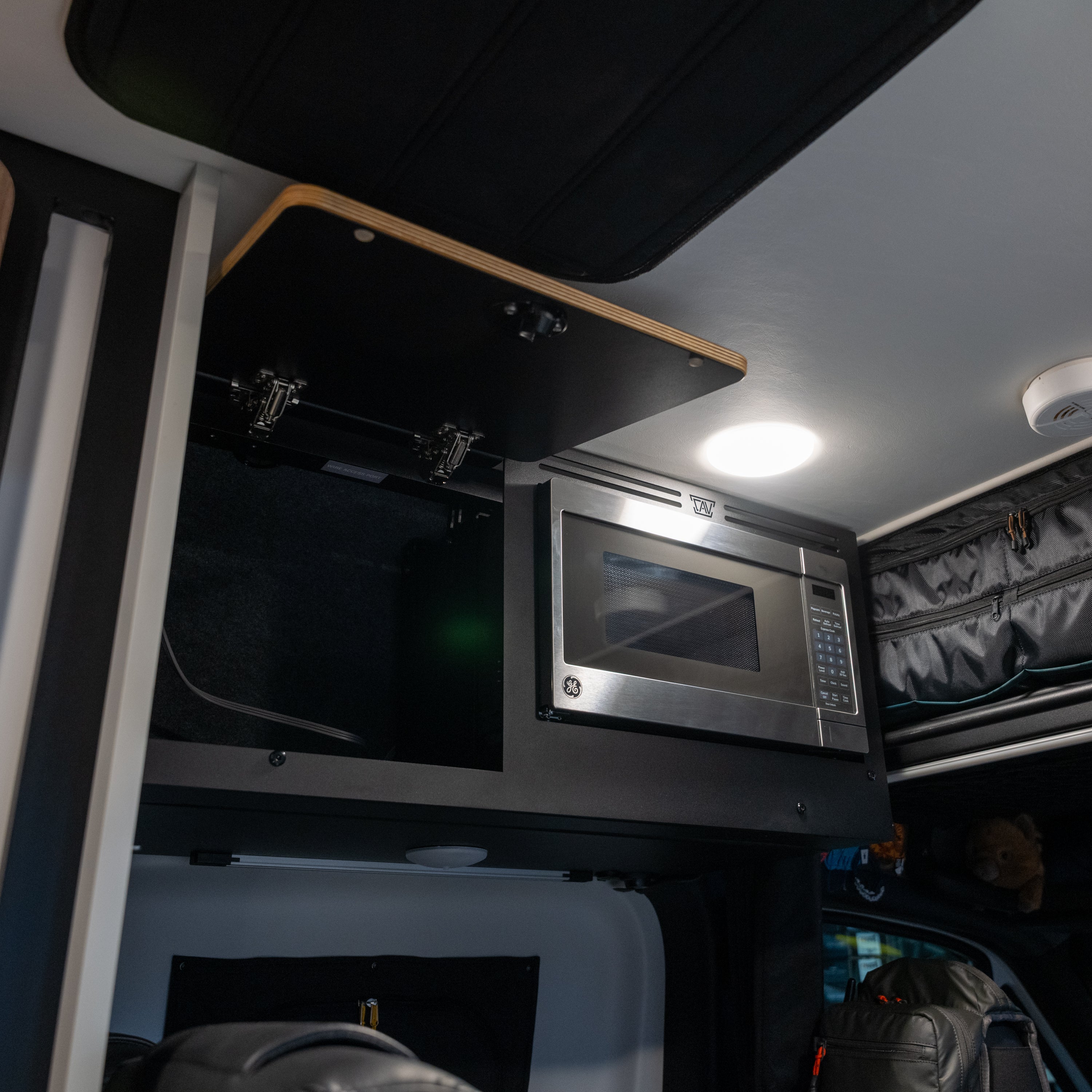 Open upper cabinet in a van showing the GH1 microwave kit installed next to storage space.