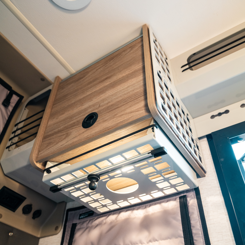 Under cabinet shelf on passenger side of van interior with wood finish and vented metal sides.