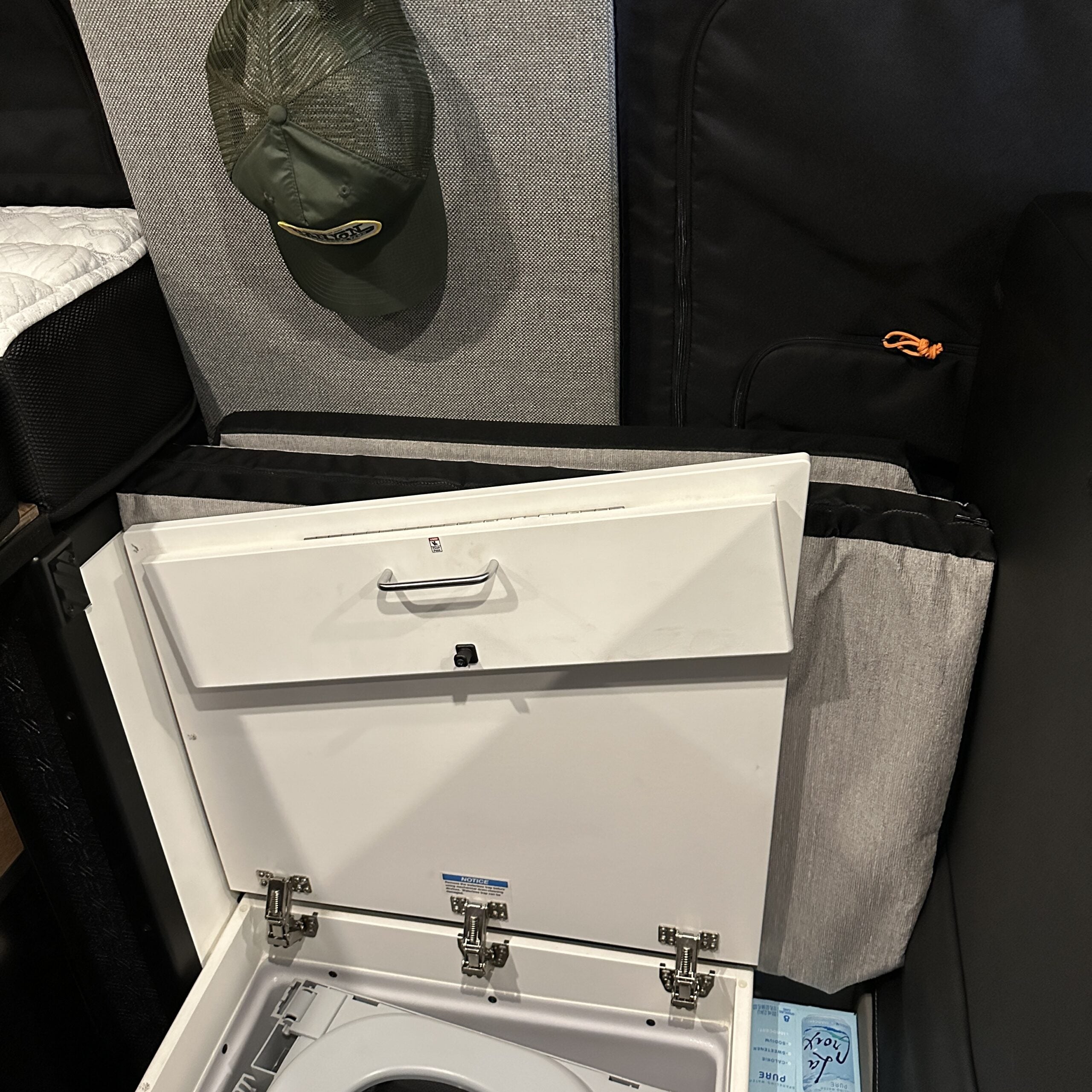 Groove Lounge Mattress Topper for Storyteller van shown stored behind bench with adjacent toilet compartment open.
