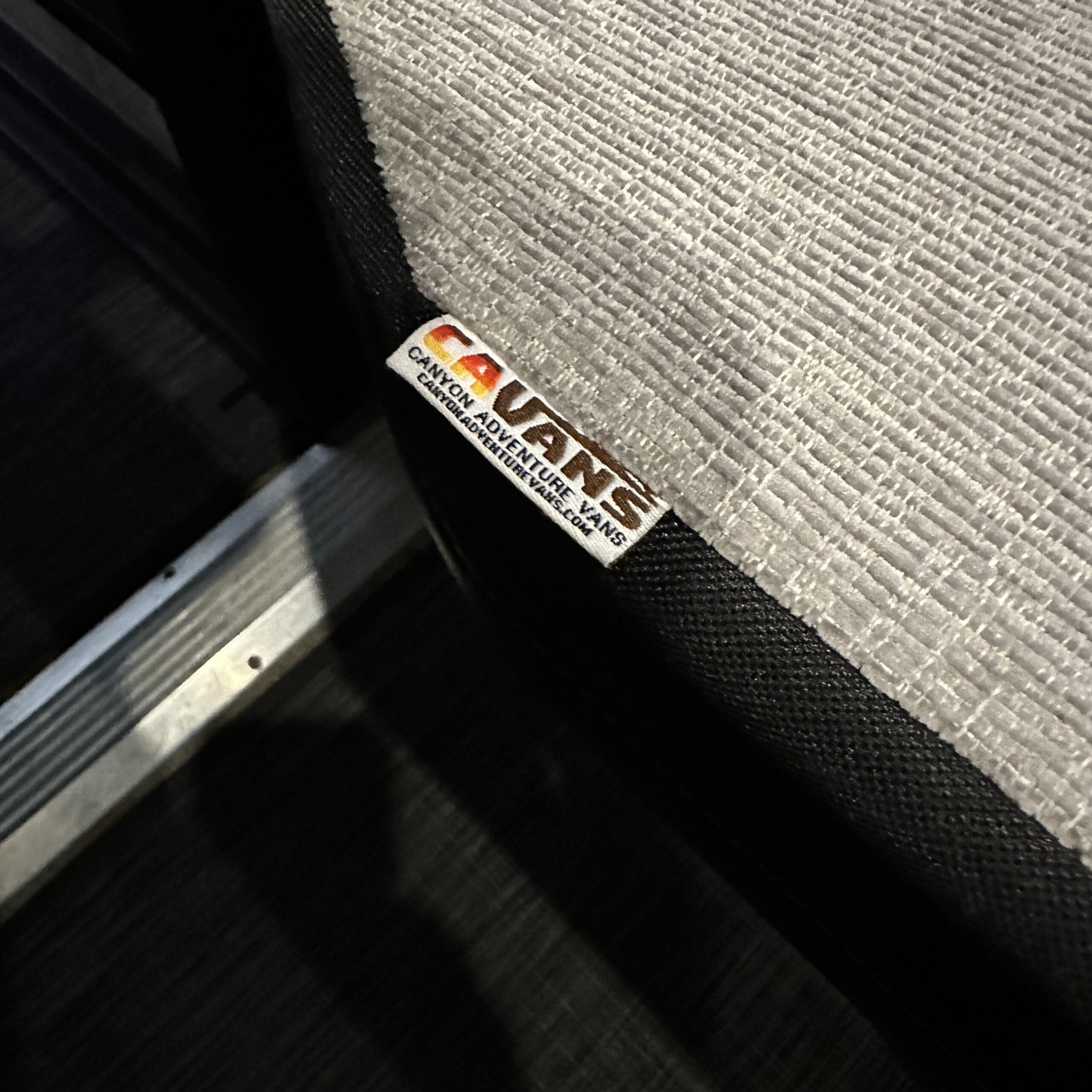 Close-up of CAV adjustable van mattress topper corner on a textured van seat.