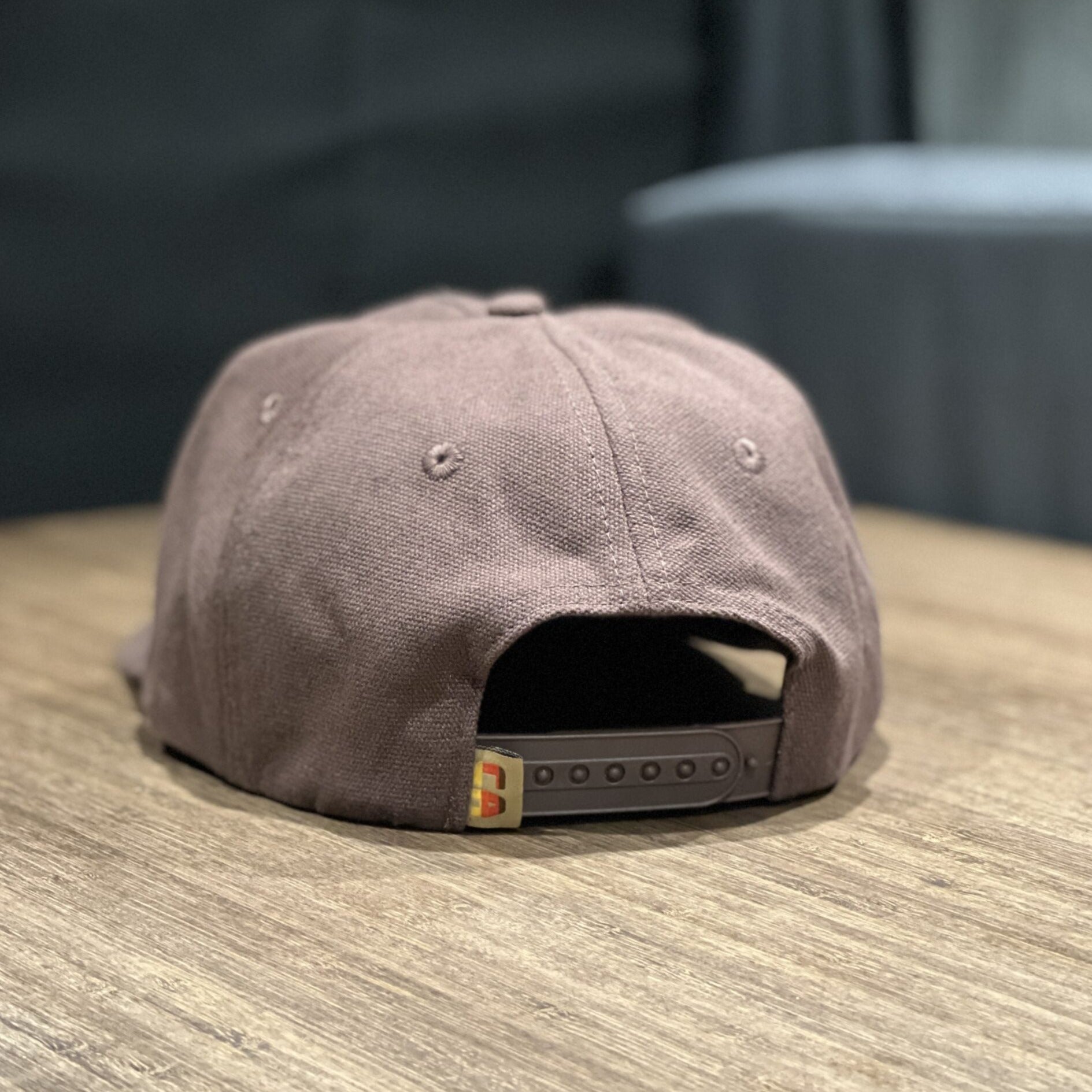 Back view of the Letterman Hat with adjustable snap closure on a wooden table