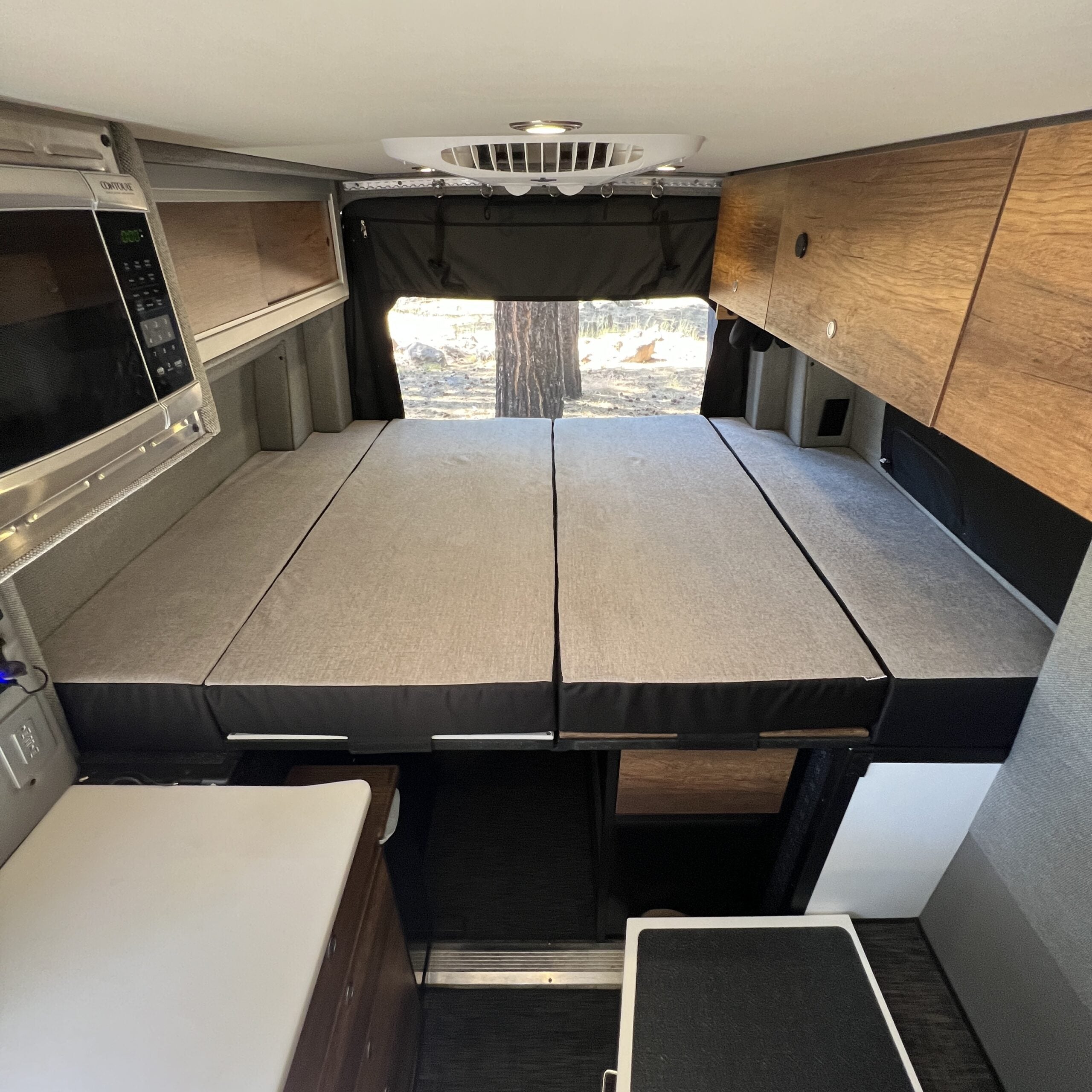 Storyteller Luxe5 cooling memory foam mattress set up in van interior with overhead cabinets and microwave.