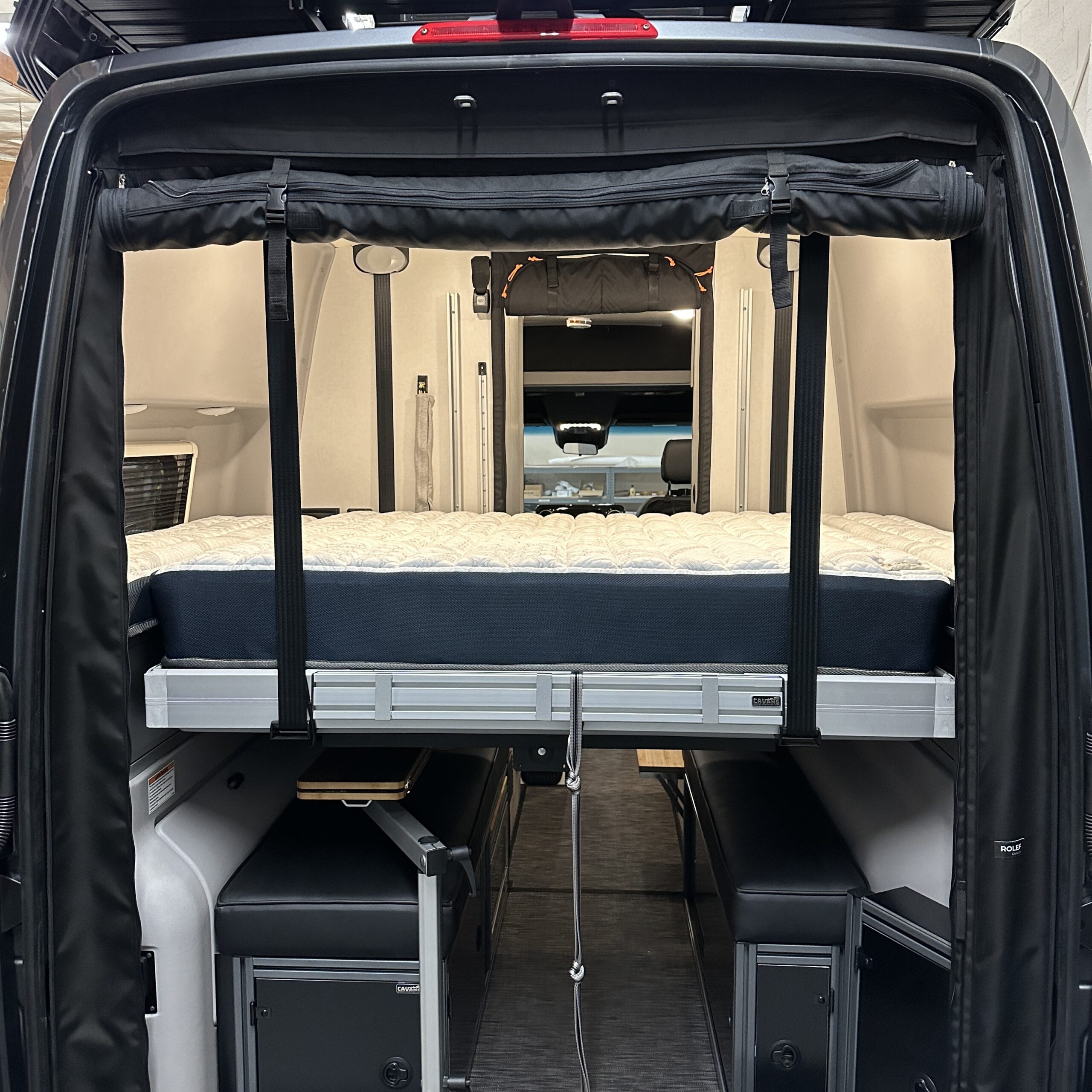 Rear view of van interior showing ULTRA Luxe Mattress elevated on a platform bed frame above storage units.