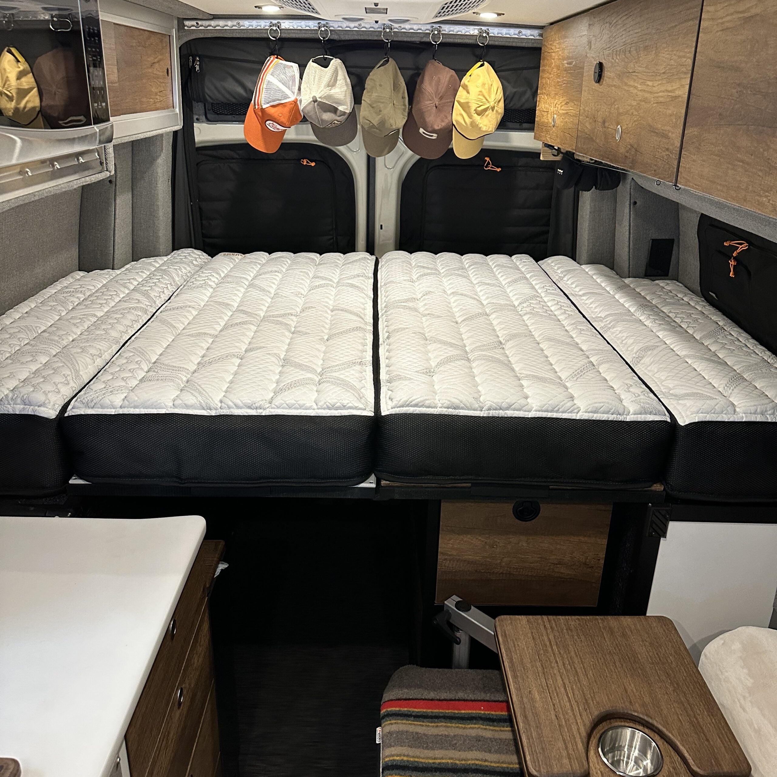 Storyteller Overland Dream Bundle mattress fully setup in van interior with wood cabinetry and hats hanging in back.