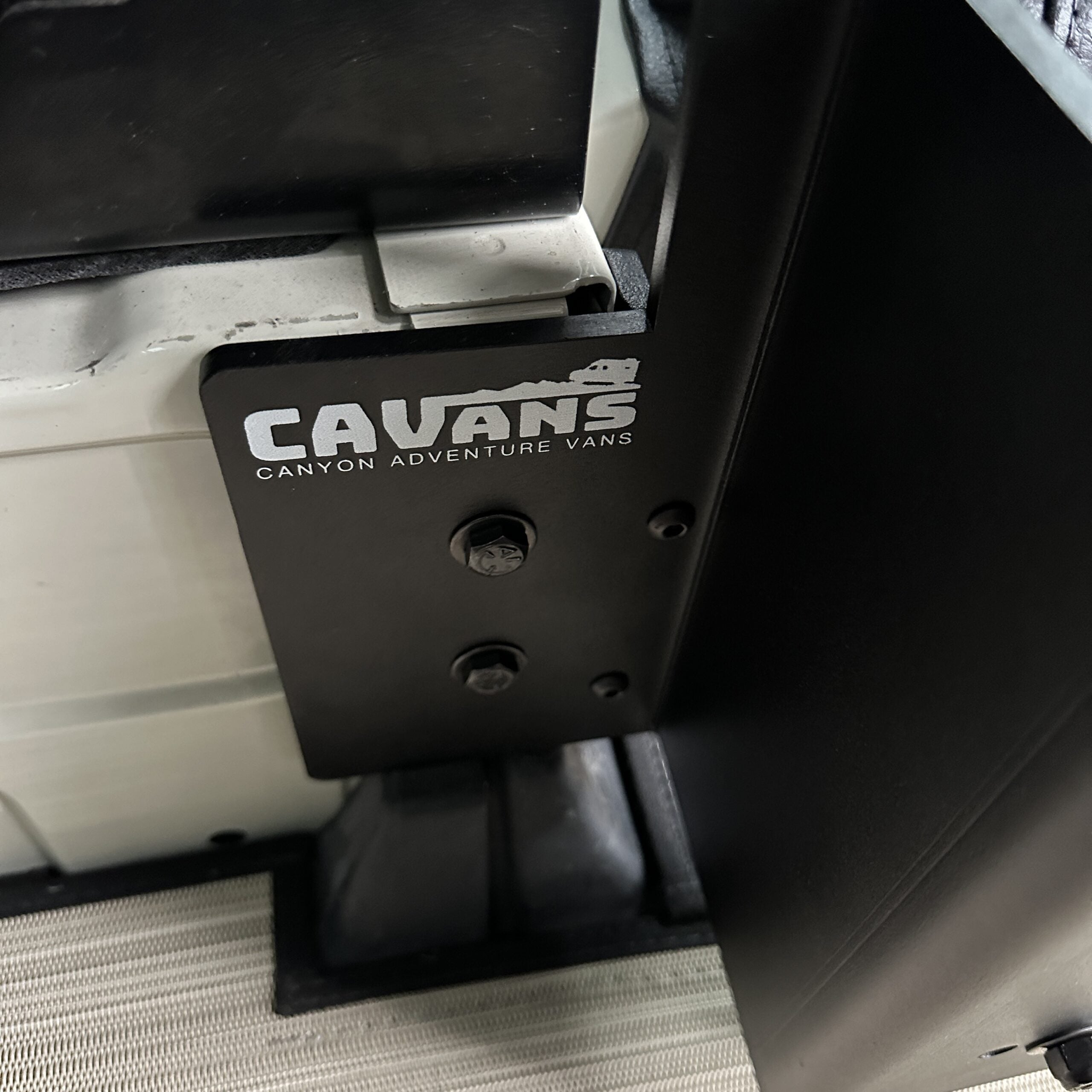 Close-up of CAVANS mounting bracket on carbon black folding table in a Revel van interior.