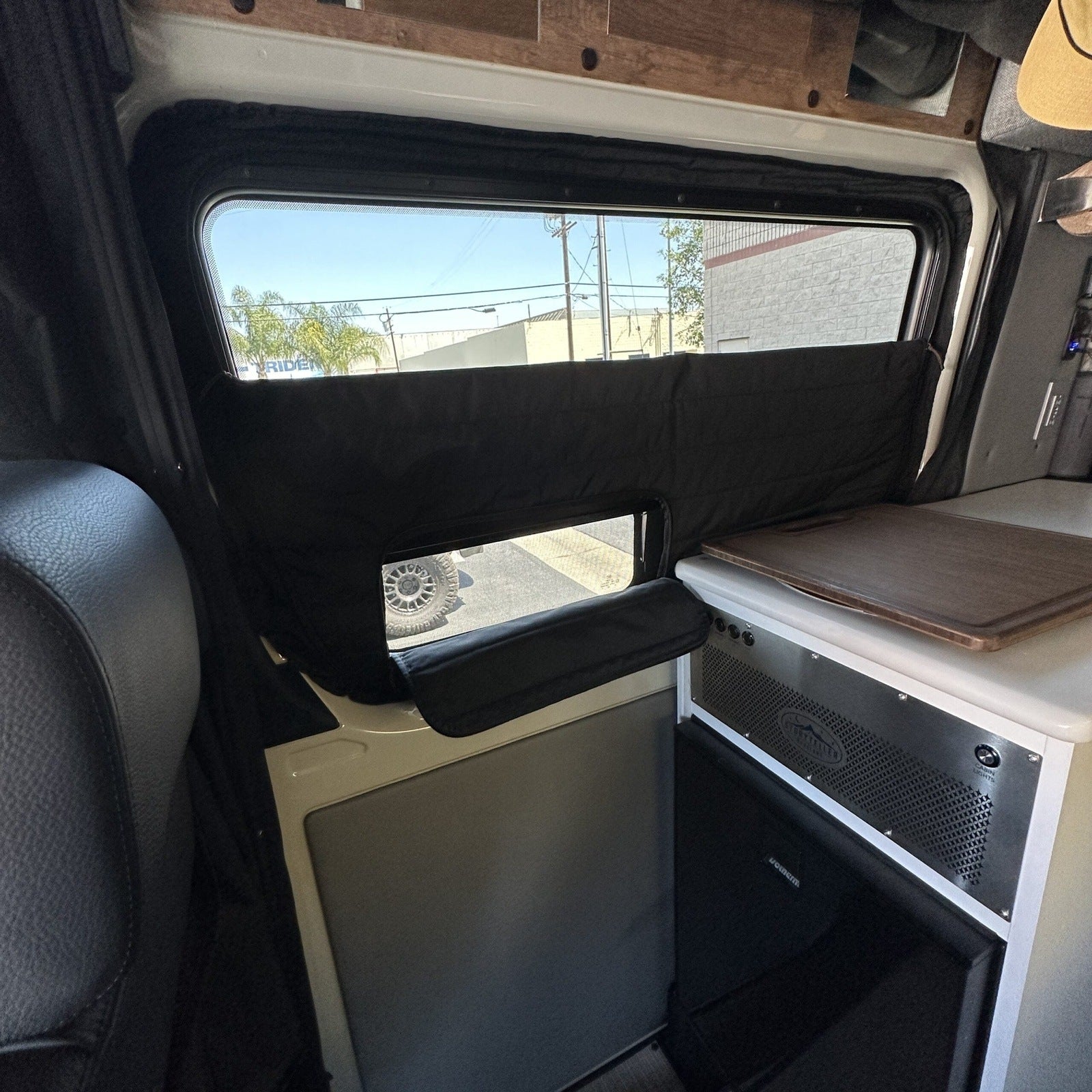 Revel Clima-Shade covering rear window inside van with counter and fridge visible.