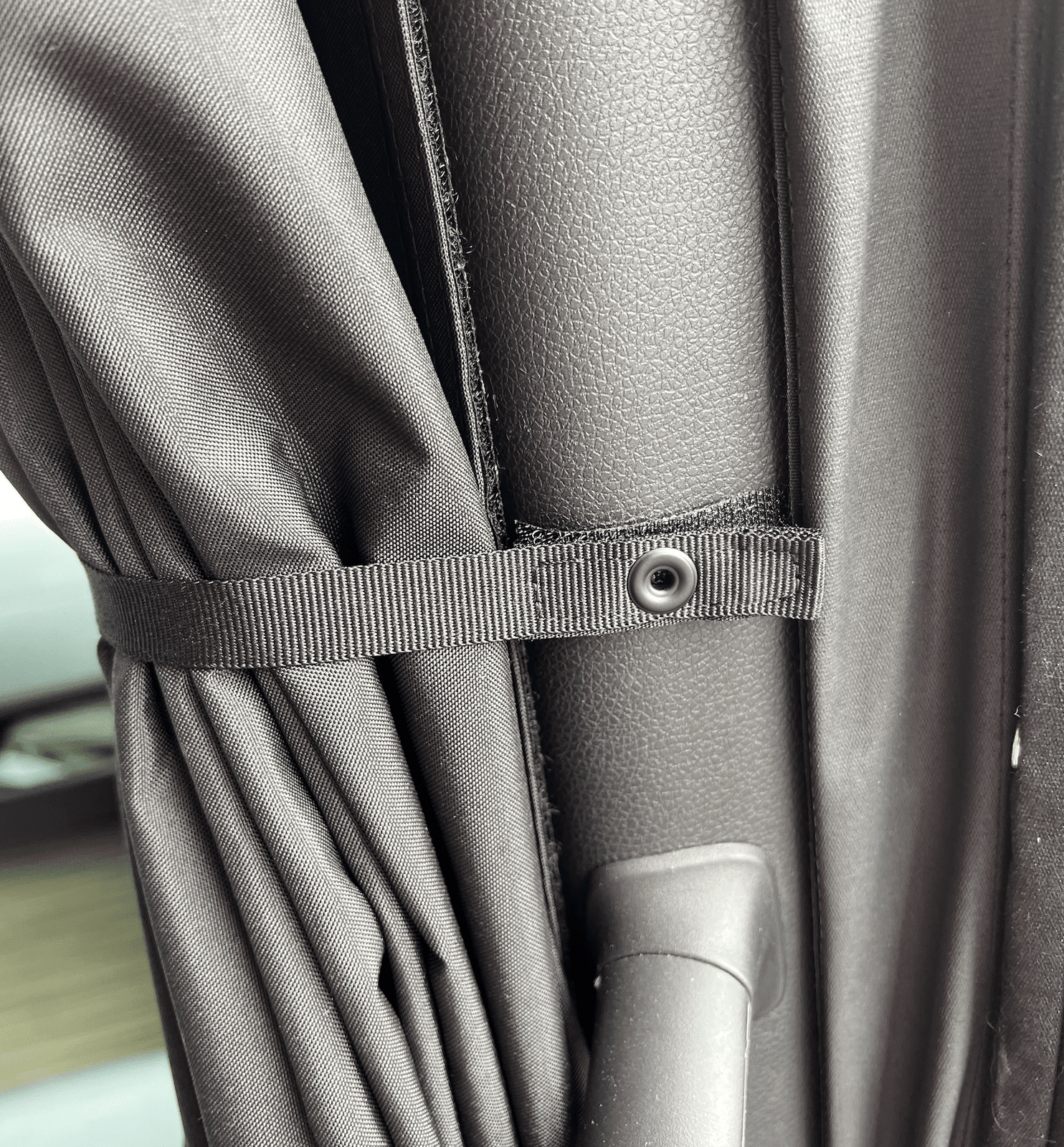 Close-up of a black curtain strap secured by a snap button inside a van door frame.