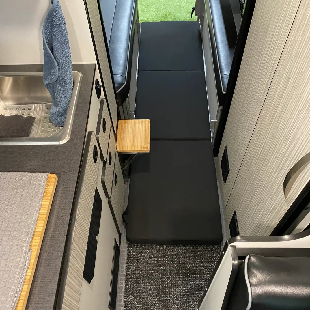Folded black floor mattress laid out in center aisle of van interior with kitchenette and seating area.