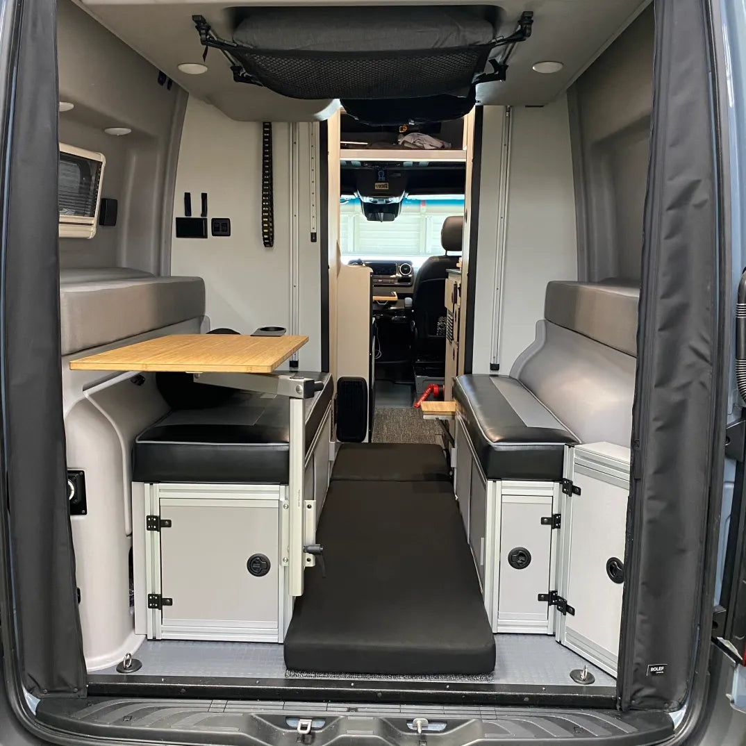 Revel floor mattress laid out between benches in a modern van interior with fold-out table.