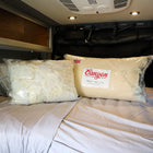 Two Dream Collection adjustable pillows in plastic packaging on a made bed inside a van.