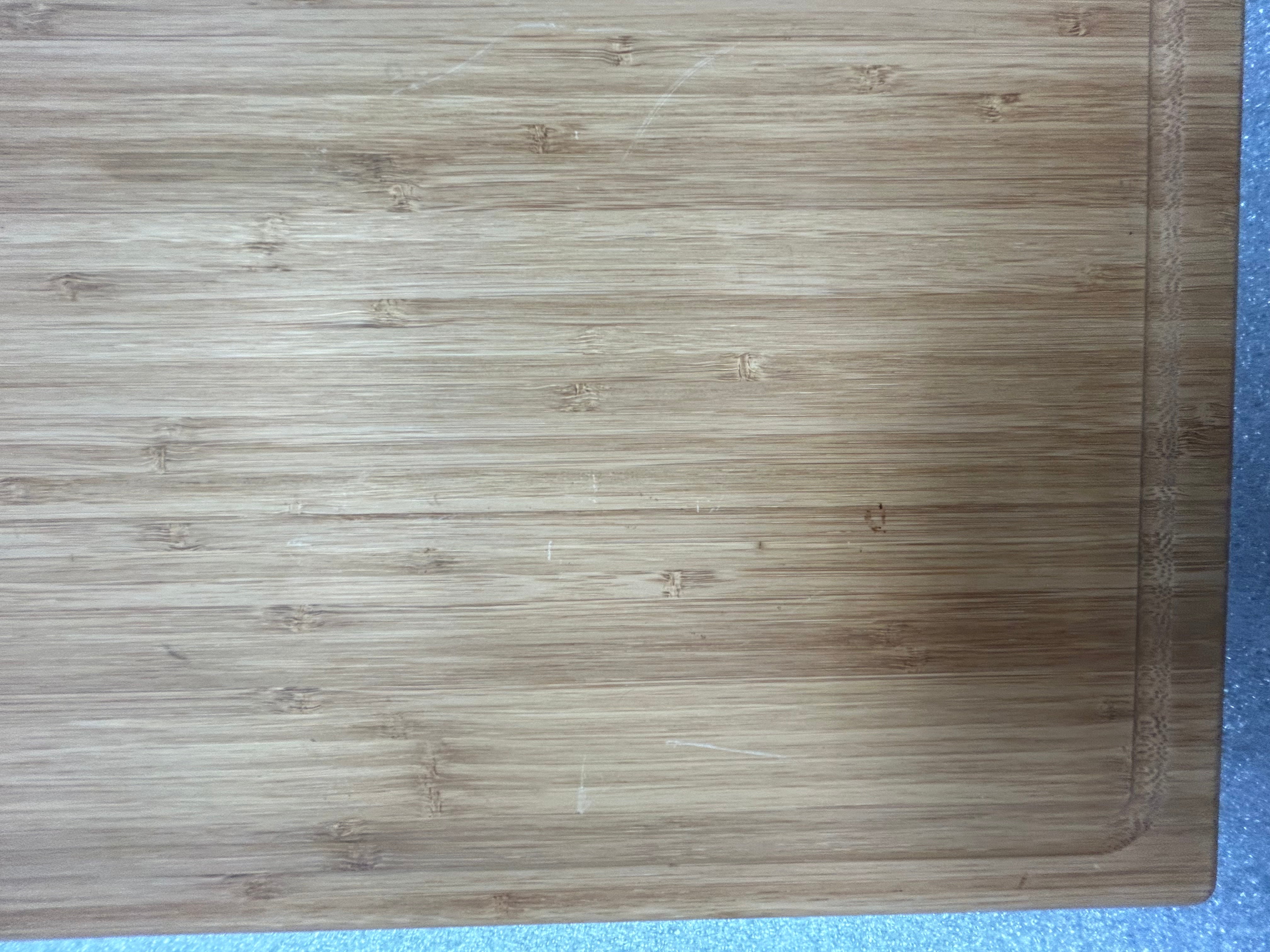 Corner view of a smooth bamboo cutting board with subtle wood grain texture.