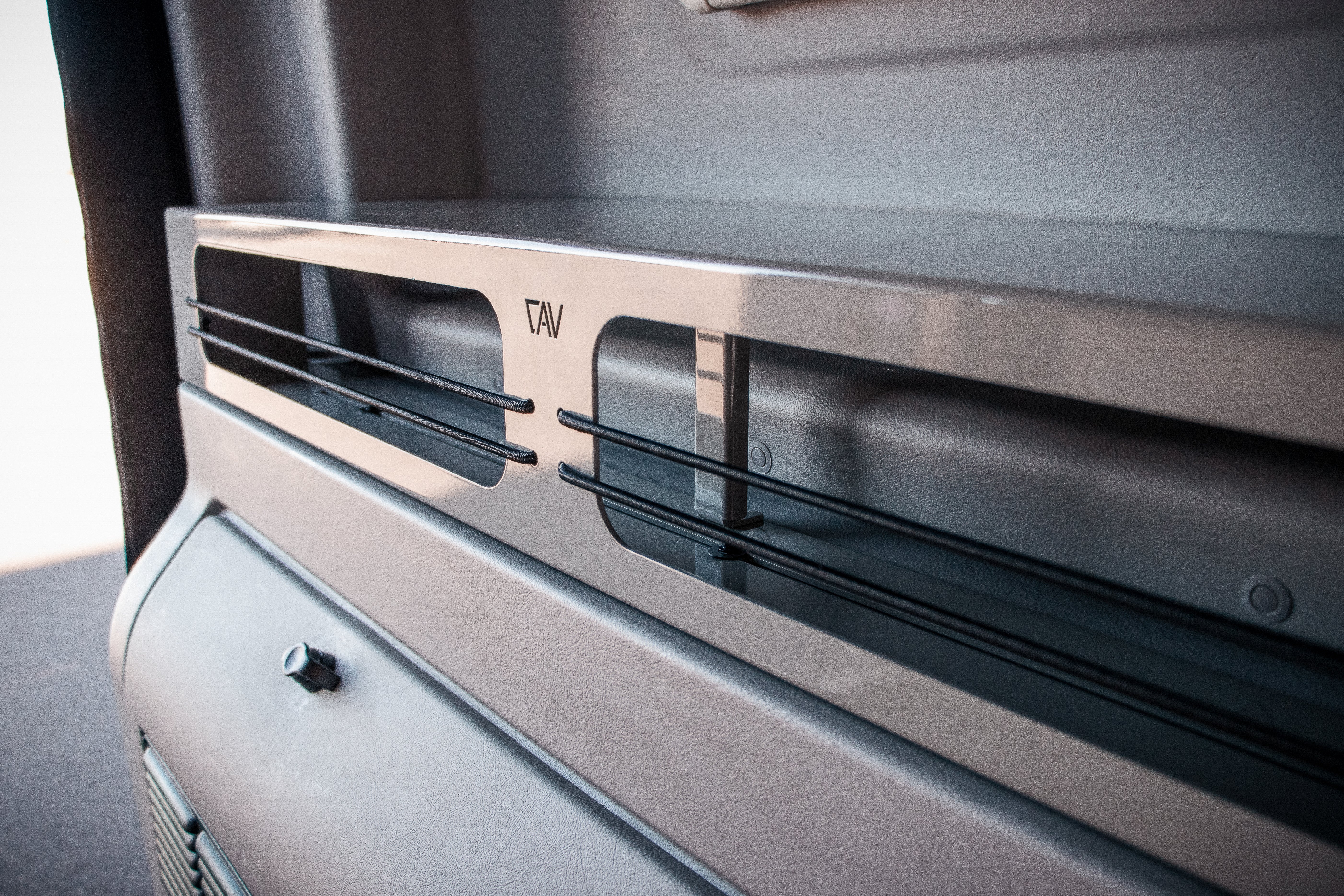 CAV vent shelf with elastic cords installed inside a van for added storage.