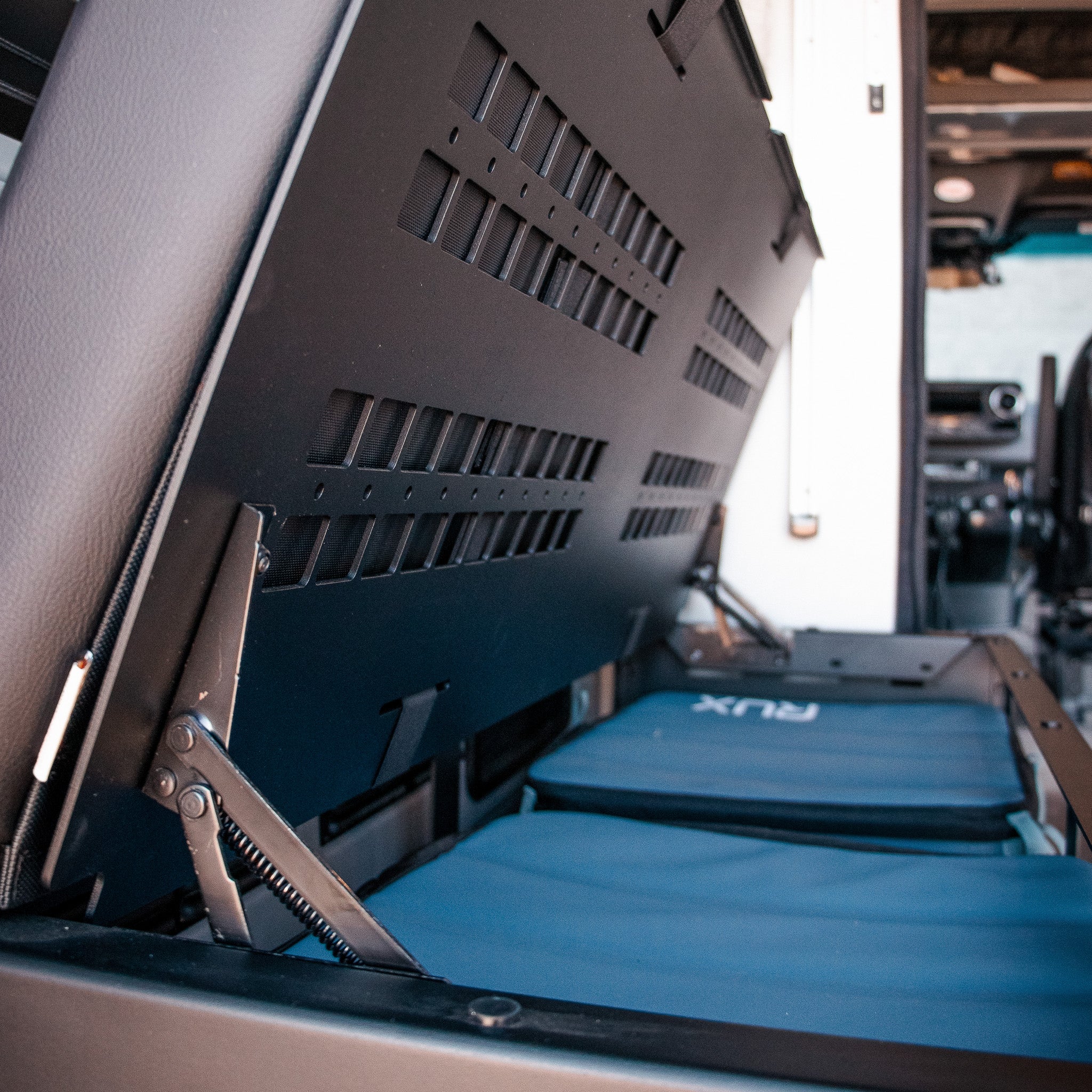 GLSS Rux folding seat and storage system inside a van, partially lifted to show compartments