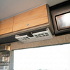 Storyteller undercabinet shelf on driver side of van interior with light wood storage panel above.