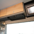 Storyteller undercabinet shelf on the driver side of a van interior with wood and fabric finishes