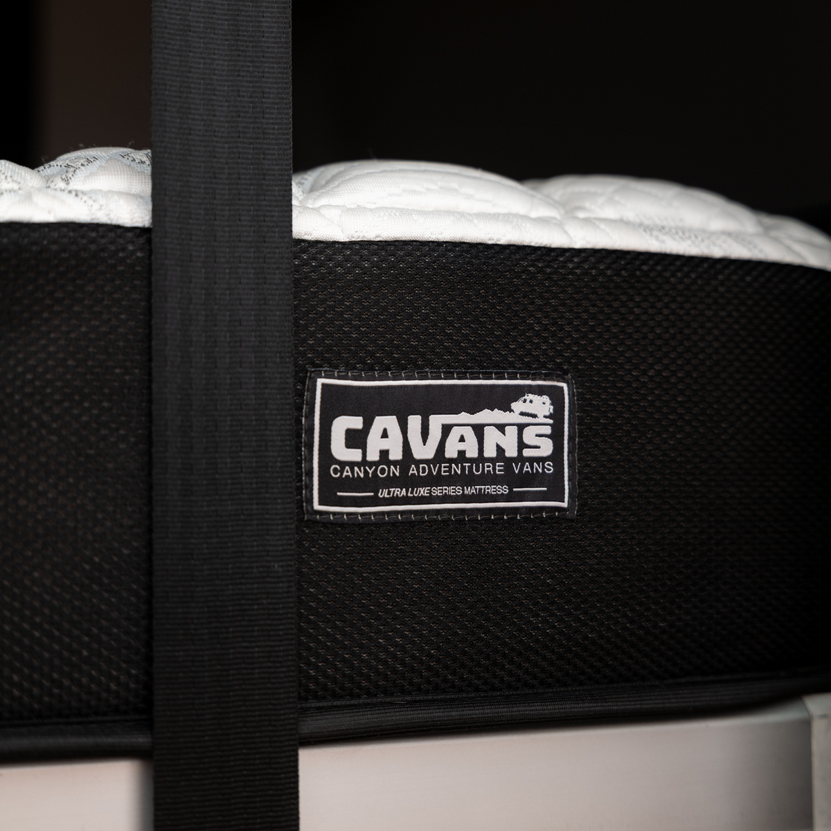 Close-up of CAVANS Ultra Luxe Series mattress edge with Canyon Adventure Vans label in van interior.