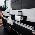 Magnetic outdoor utility shelf with paper towels and storage cups attached to side of black and white van.