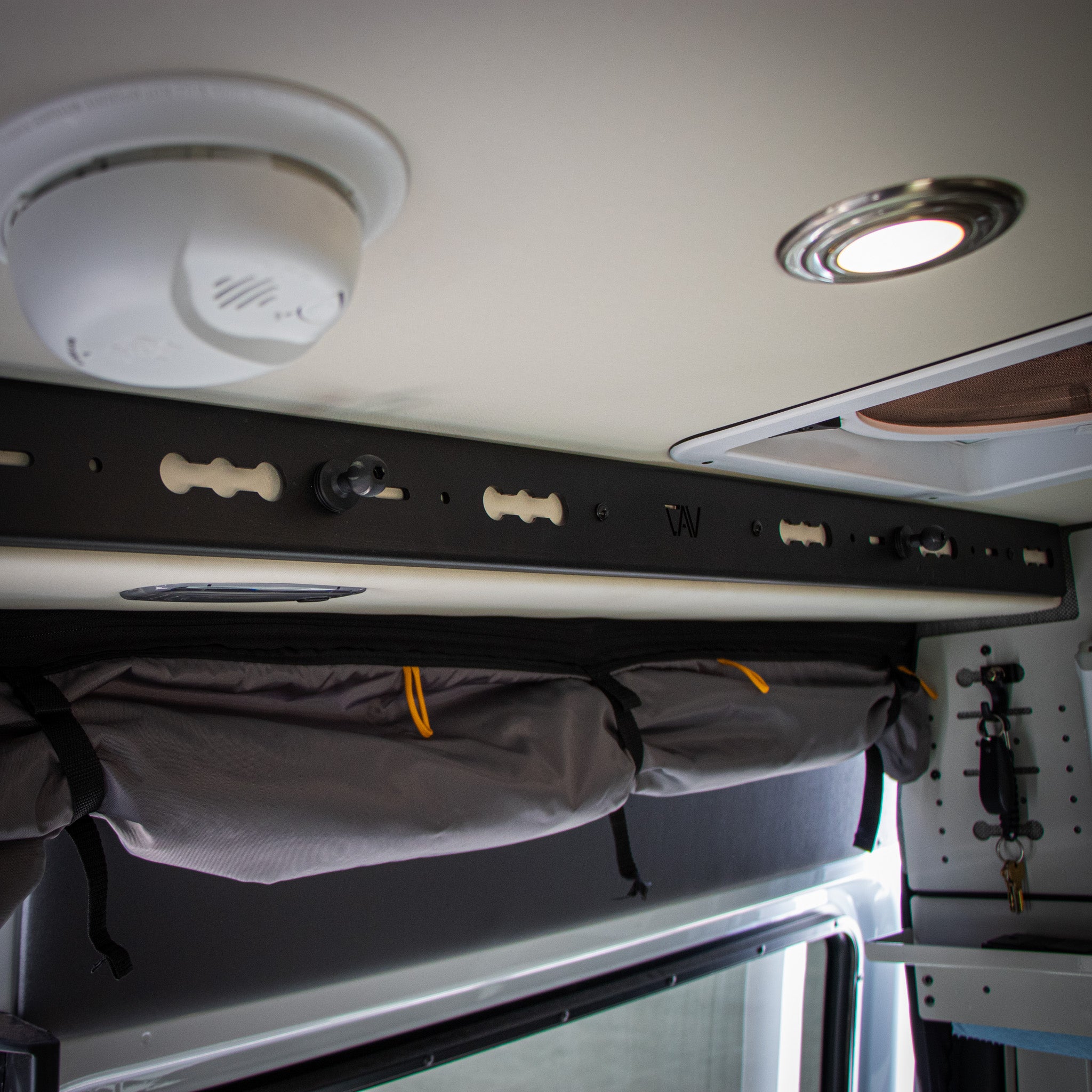 Interior of mercedes sprinter van storyteller mode 2023 with black overhead slider door l track pro with 3 bulletpoint female balls mounted into l track slot and bug screen wrapped below and storyteller kitchen caddy beige in background with keys hanging from l track hook mounted