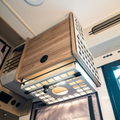 Under cabinet shelf on passenger side of van interior with wood finish and vented metal sides.