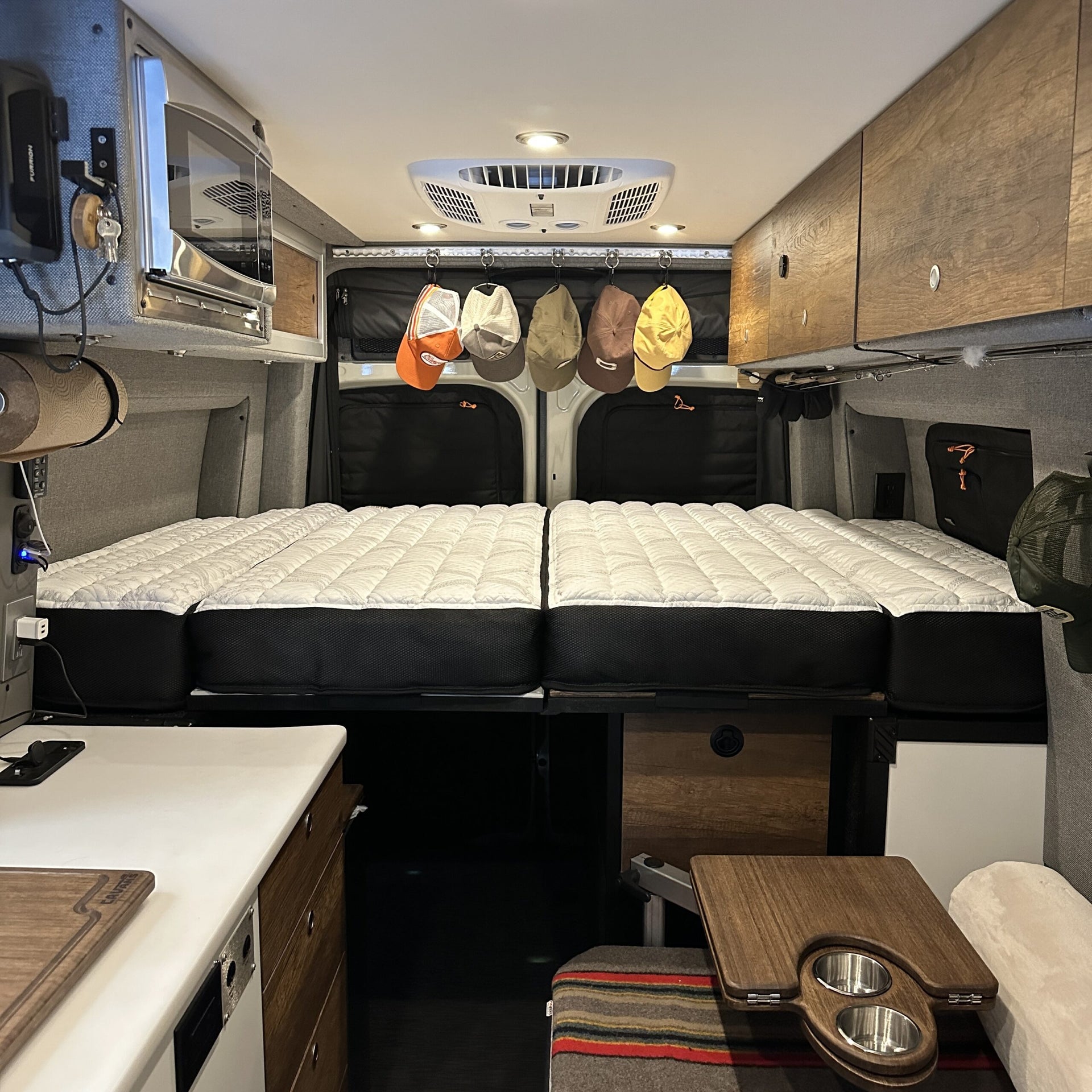 ULTRA Luxe Mattress inside Storyteller Overland Mode LT van with wood cabinetry and hanging hats