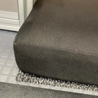 Close-up of the Revel floor mattress corner inside a van, showing dark fabric and carpeted flooring.