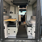 Folded Revel floor mattress in van rear cabin with seating and fold-out table visible.