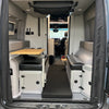 Folded Revel floor mattress in van rear cabin with seating and fold-out table visible.